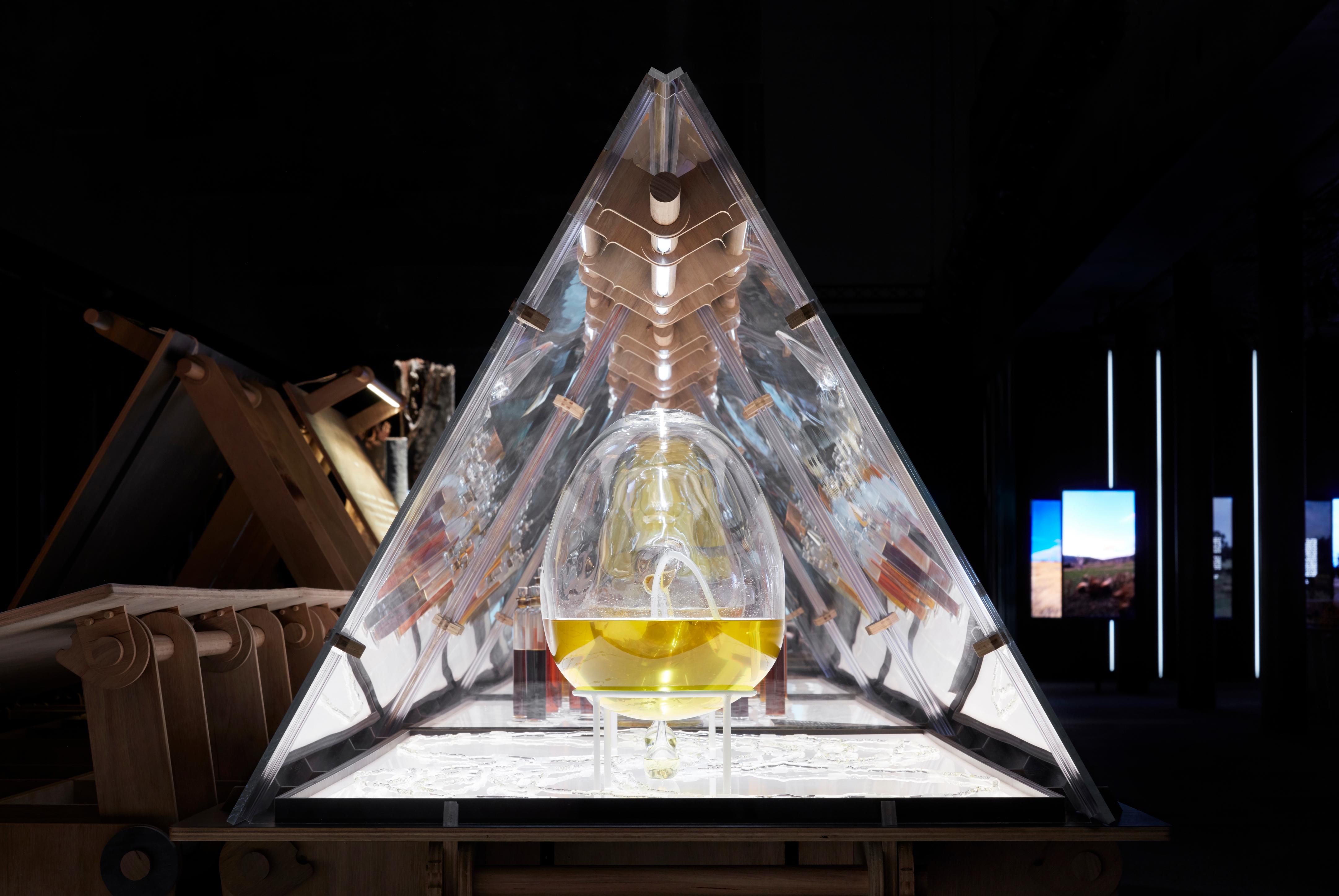 A glass pyramid seen side on with a glass globe inside filled half way with yellow oil.