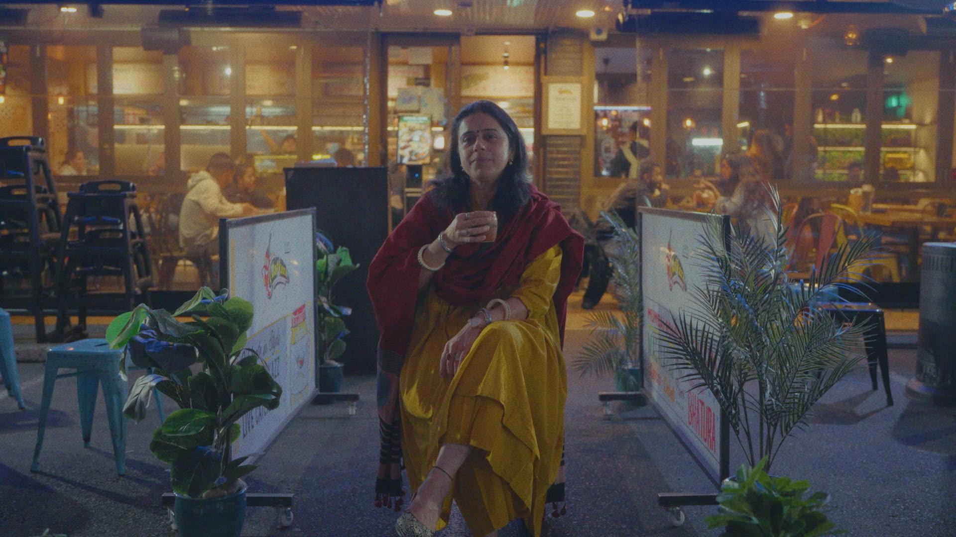 Woman holding a cup in front of her amongst restaurants.