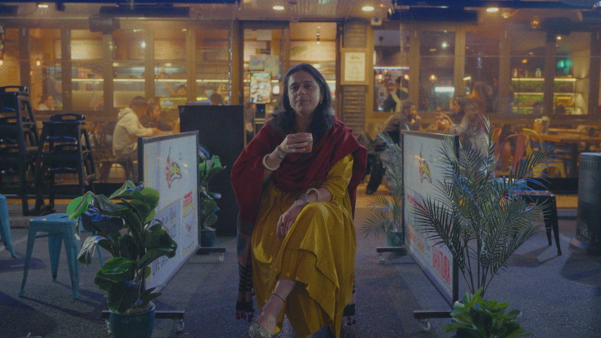 Woman holding a cup in front of her amongst restaurants.