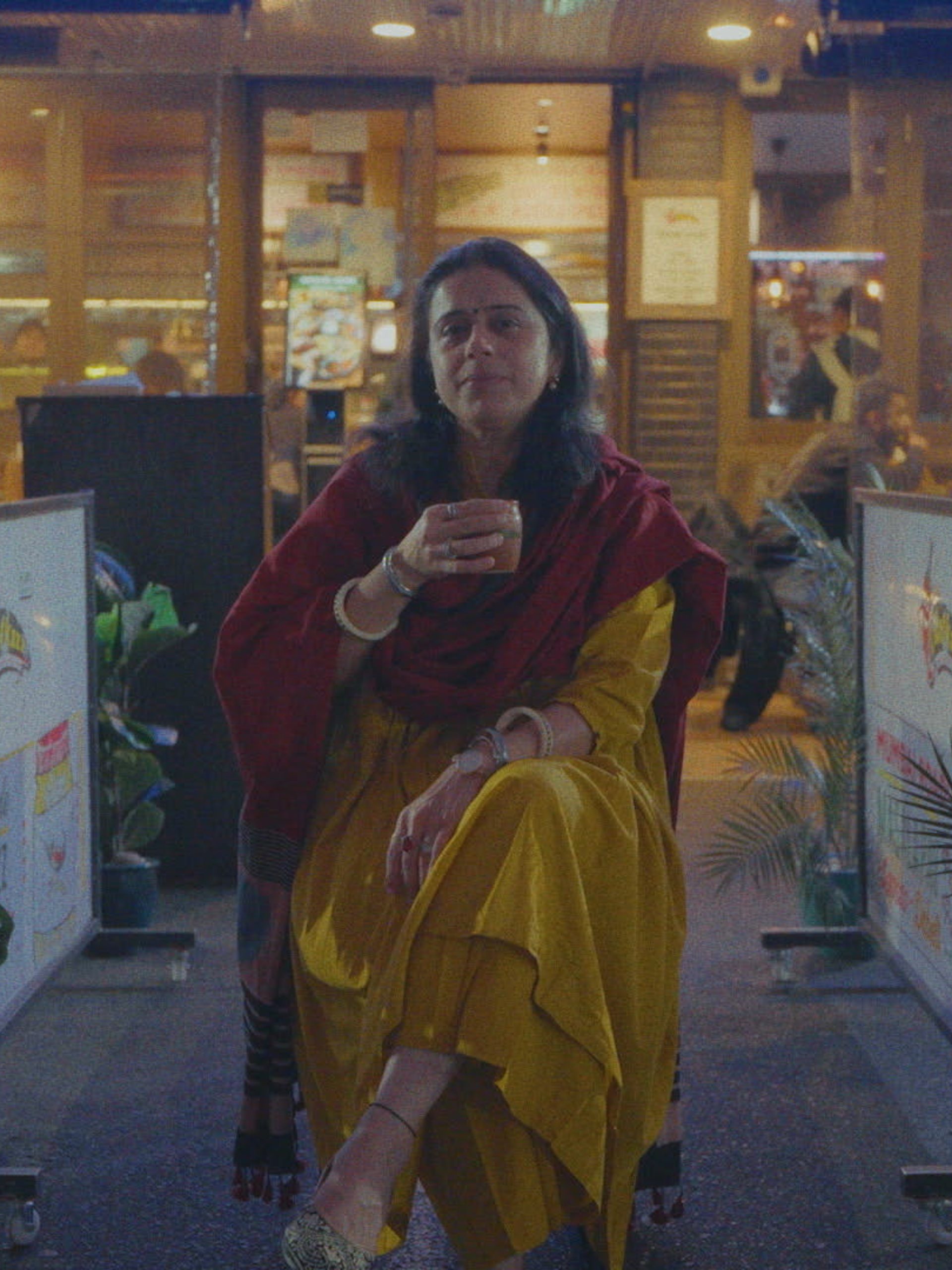 Woman holding a cup in front of her amongst restaurants.