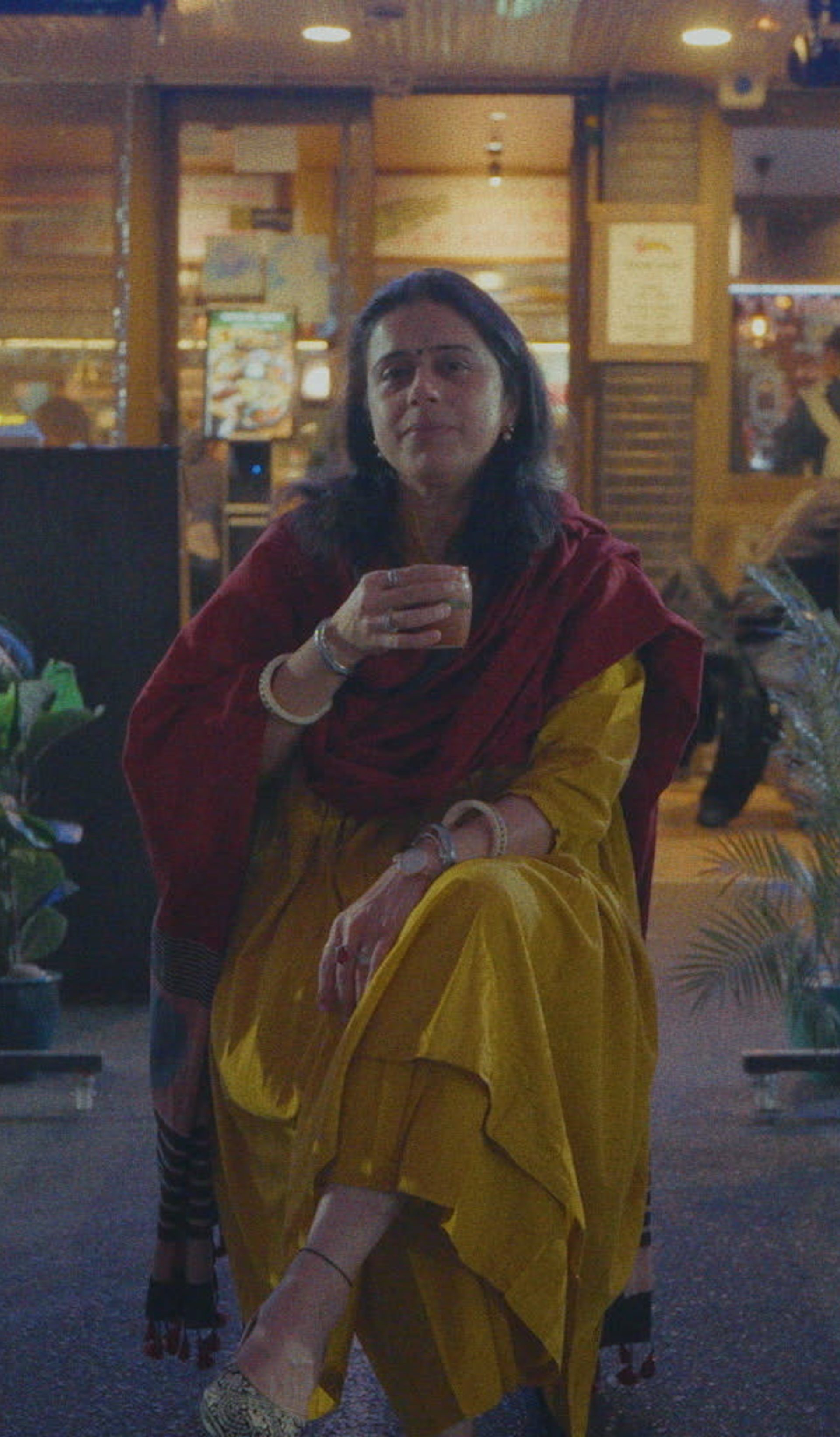 Woman holding a cup in front of her amongst restaurants.