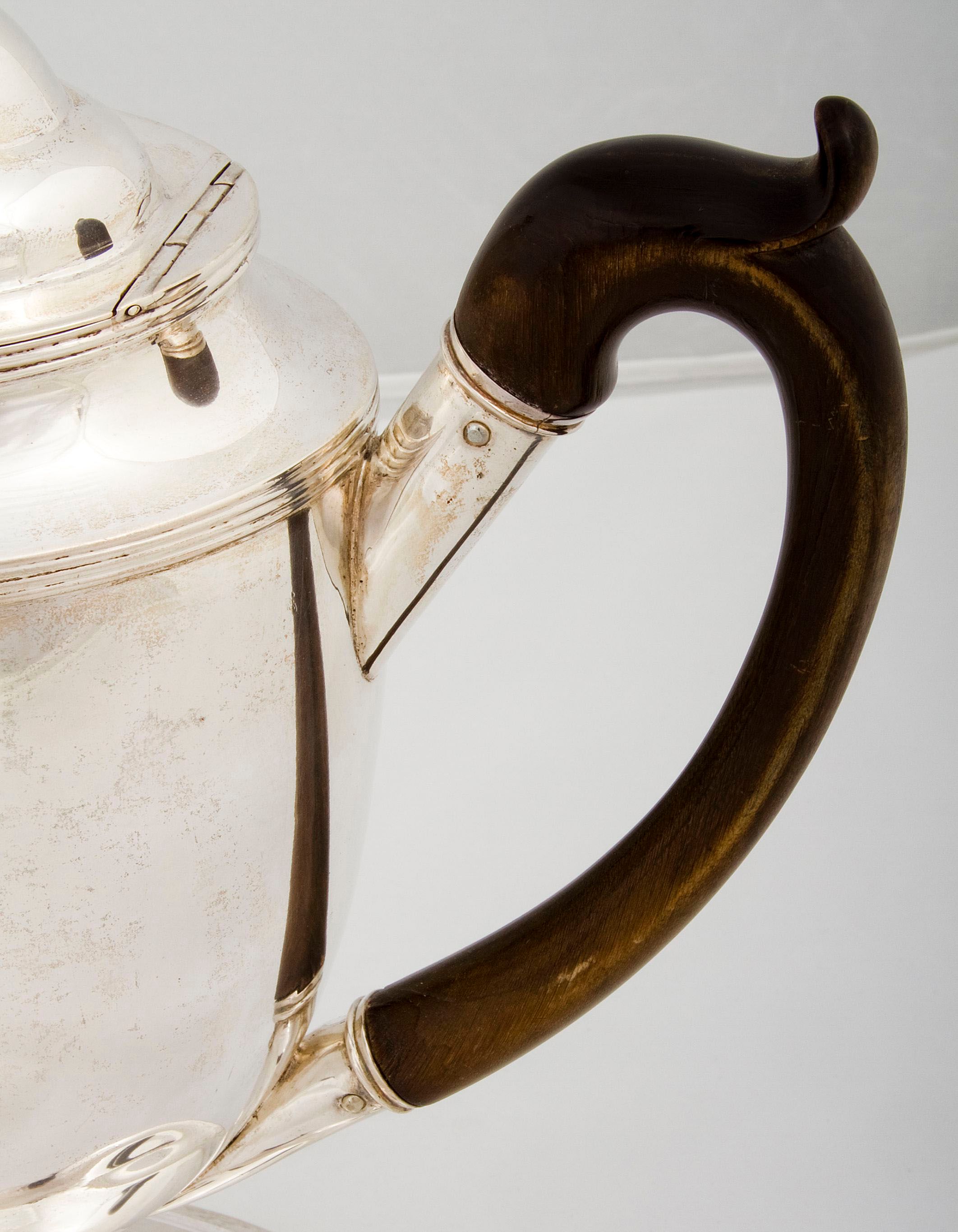 A coffee pot with lid, made of silver and wood, with a c-shaped wooden handle.