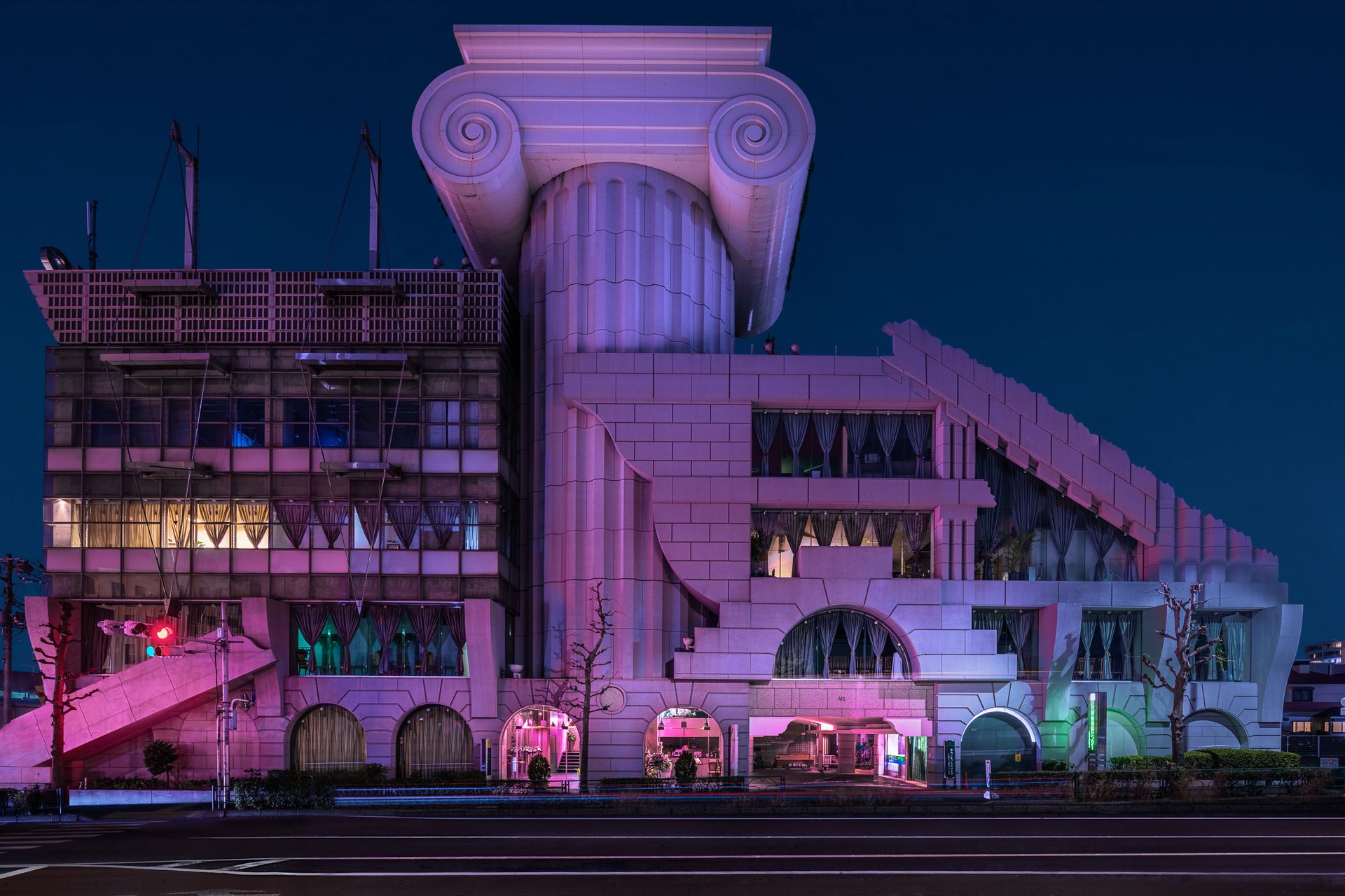A large, eclectic building at night, lit with purple lights. In the middle of the building is an oversized Ionic column.