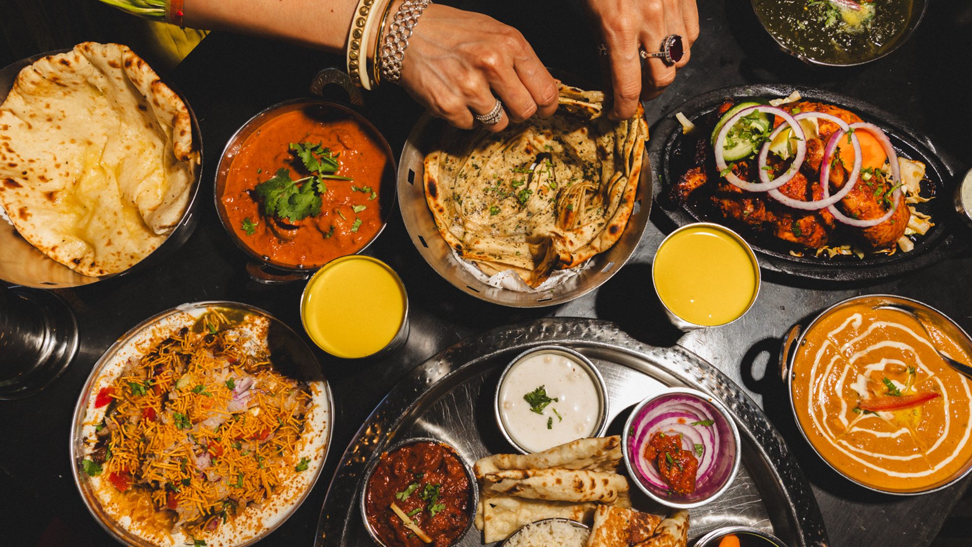 Hands reaching from a feast of food.