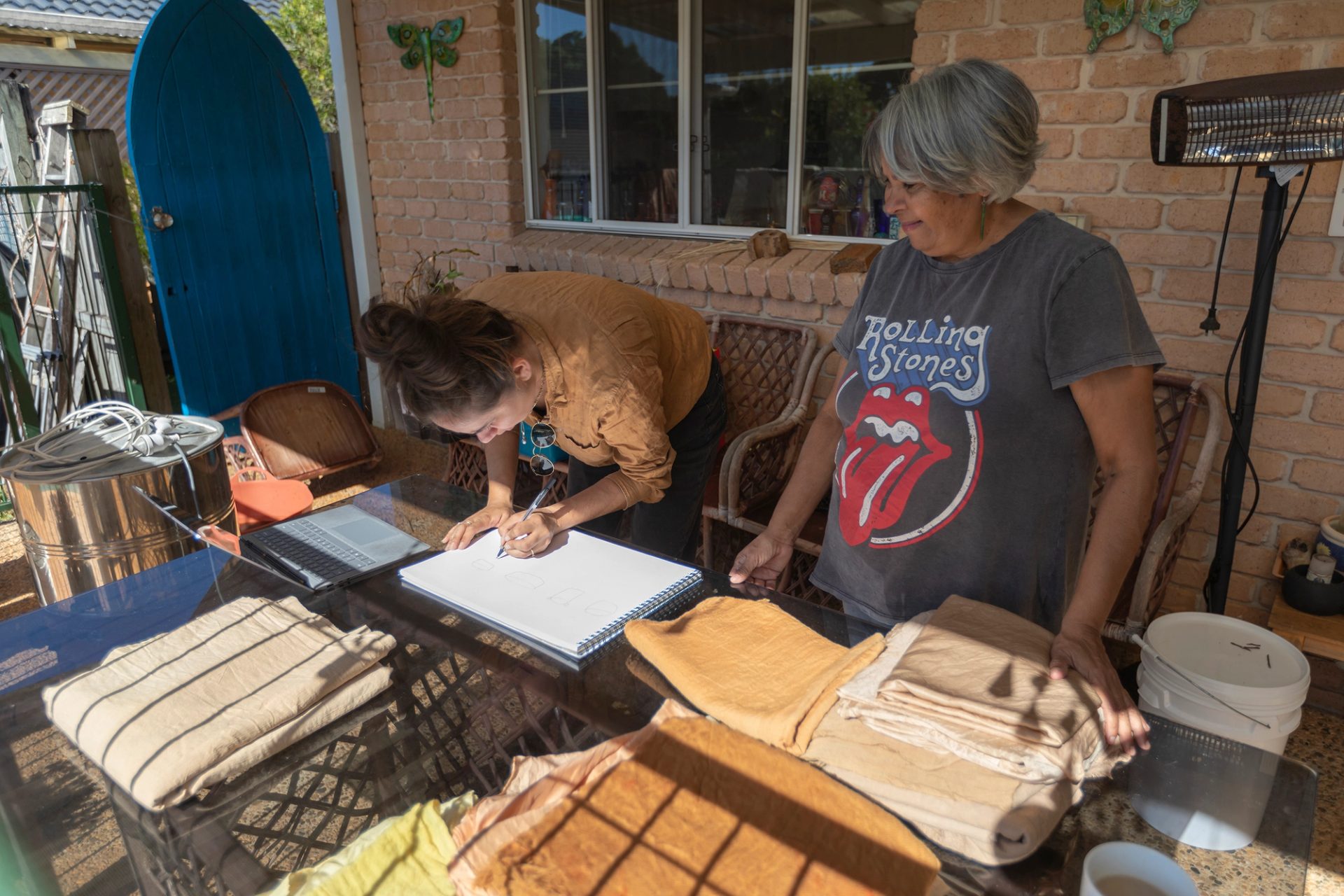Two women standing at the back of a brick house.