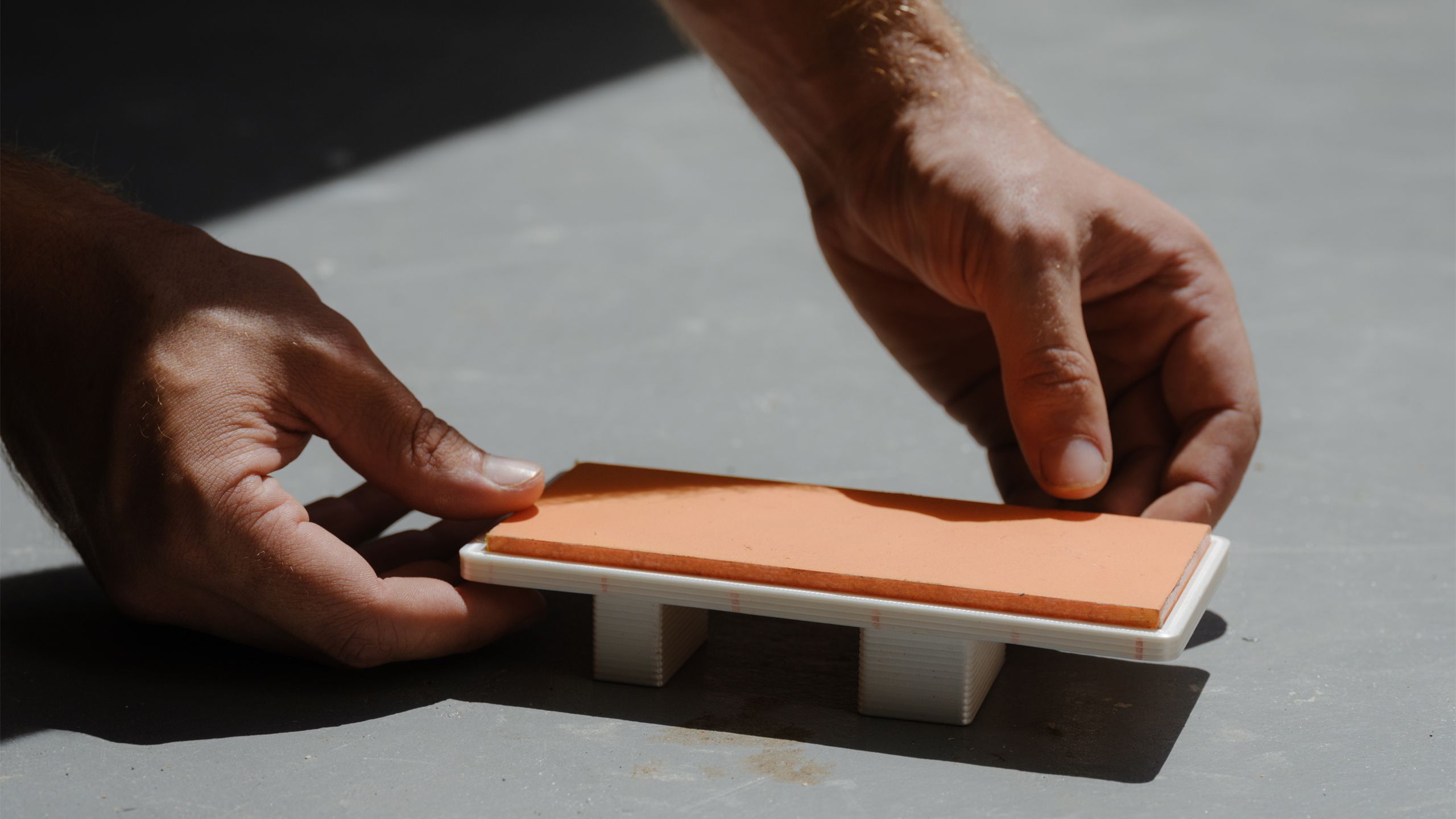 Tiny model of daybed being placed in the sun by two hands.