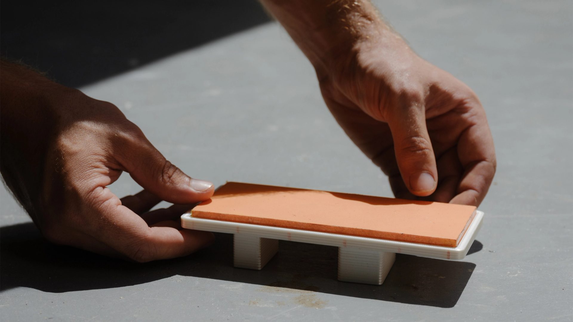 Tiny model of daybed being placed in the sun by two hands.