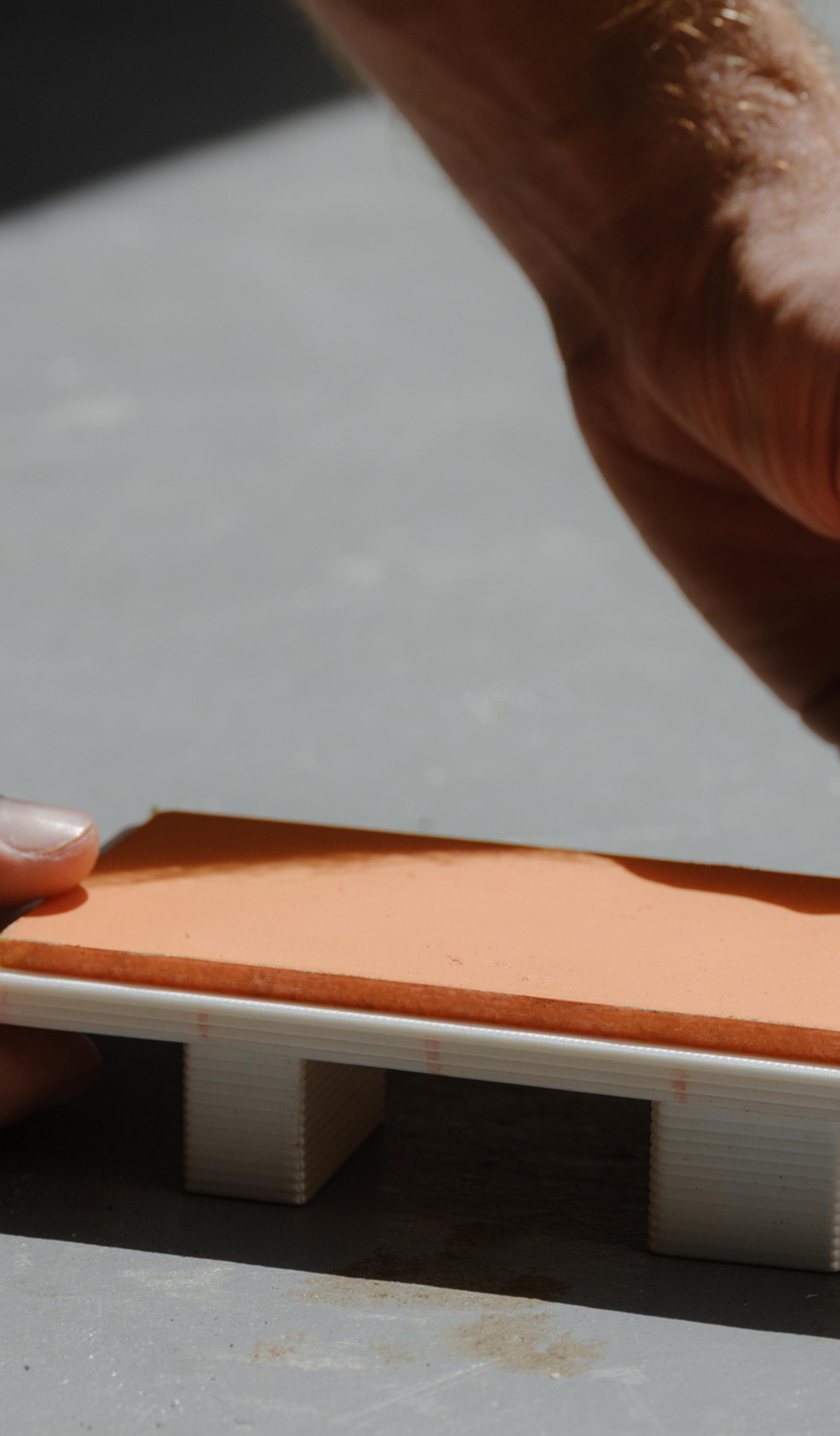 Tiny model of daybed being placed in the sun by two hands.