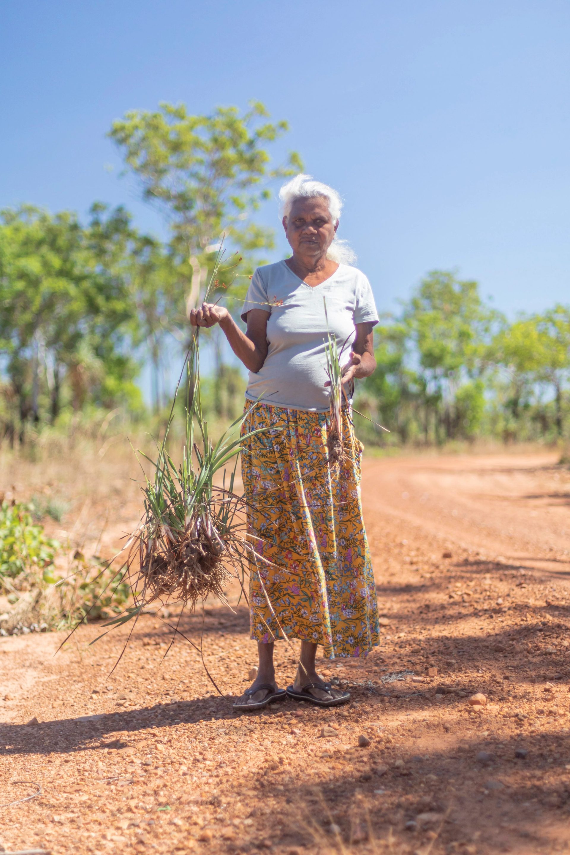 Woman stands holding plant in desert.