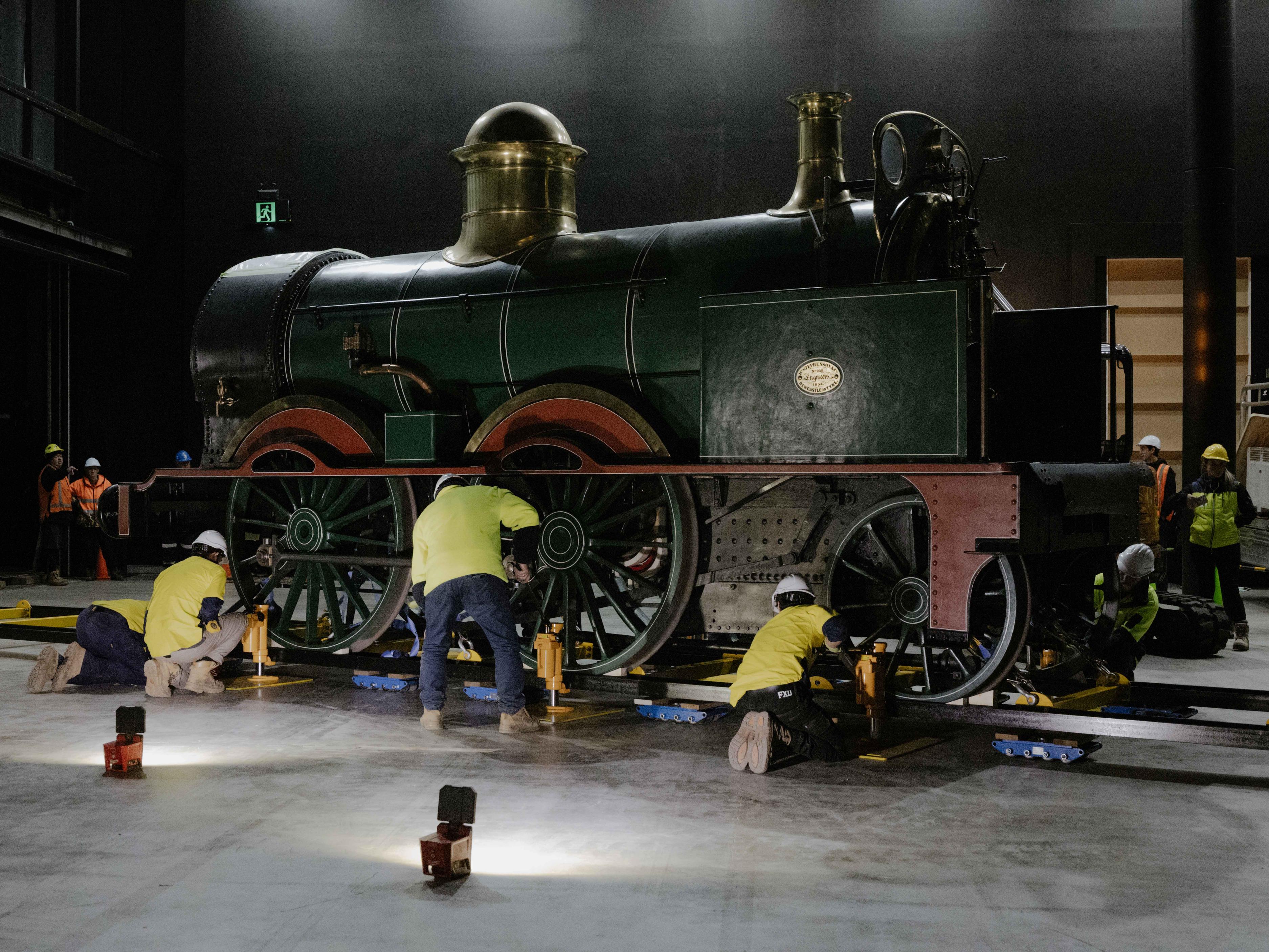 Floor lights illuminating a train with trades people at every wheel of the train.