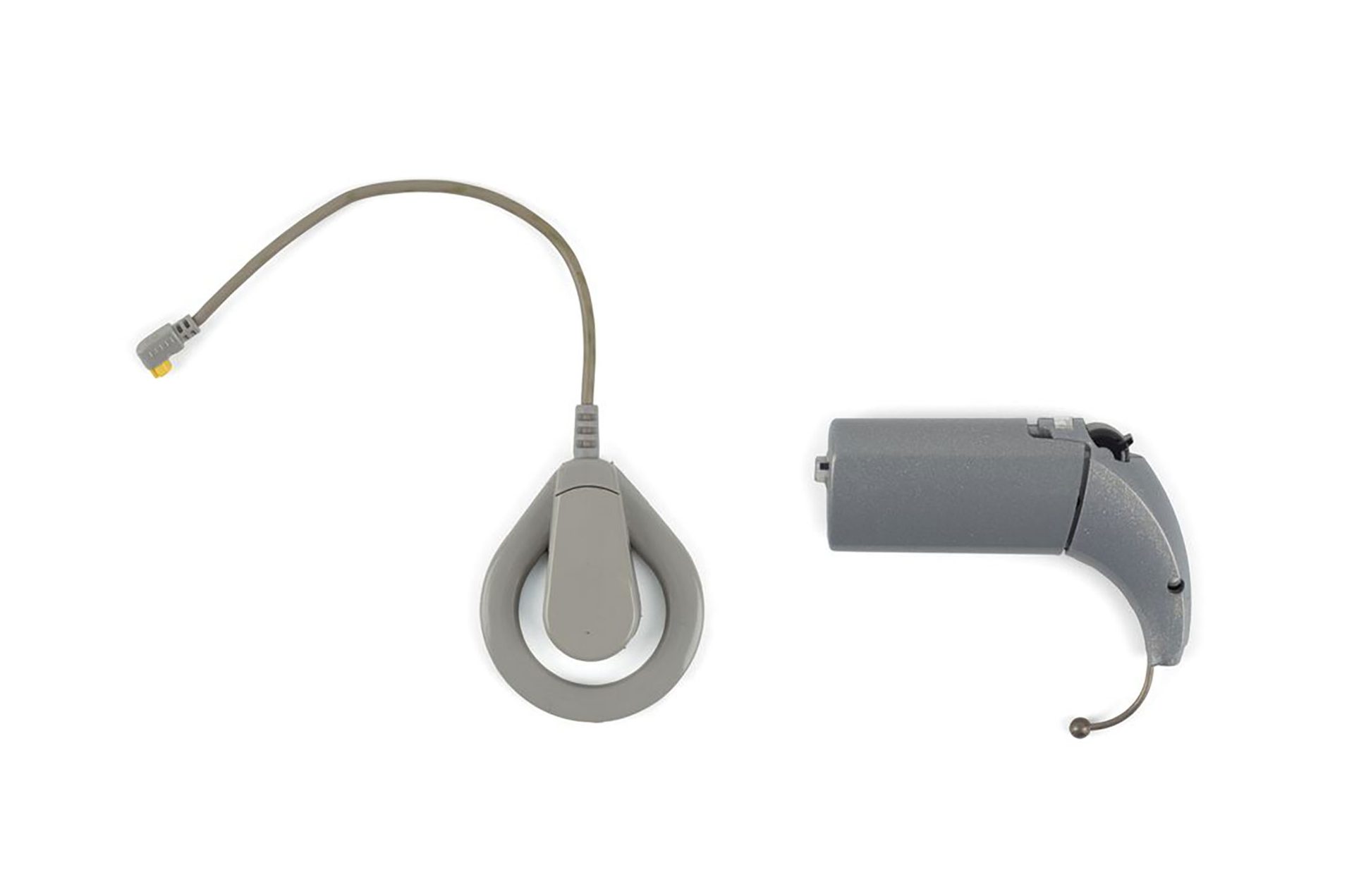 Grey cochlear implant and speech processor photographed against white background