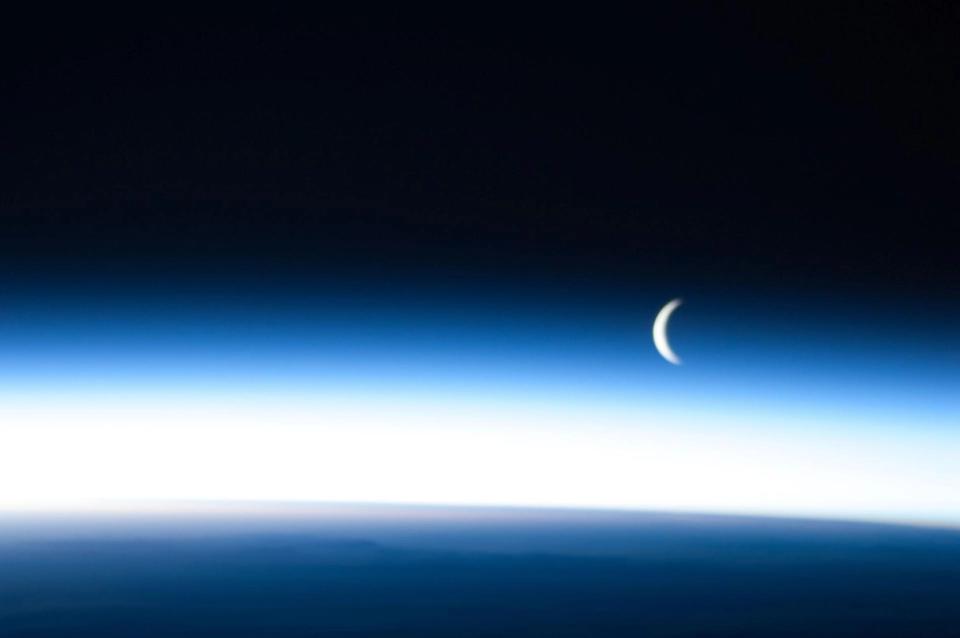 Crescent moon above Earth's atmosphere lit with blue.