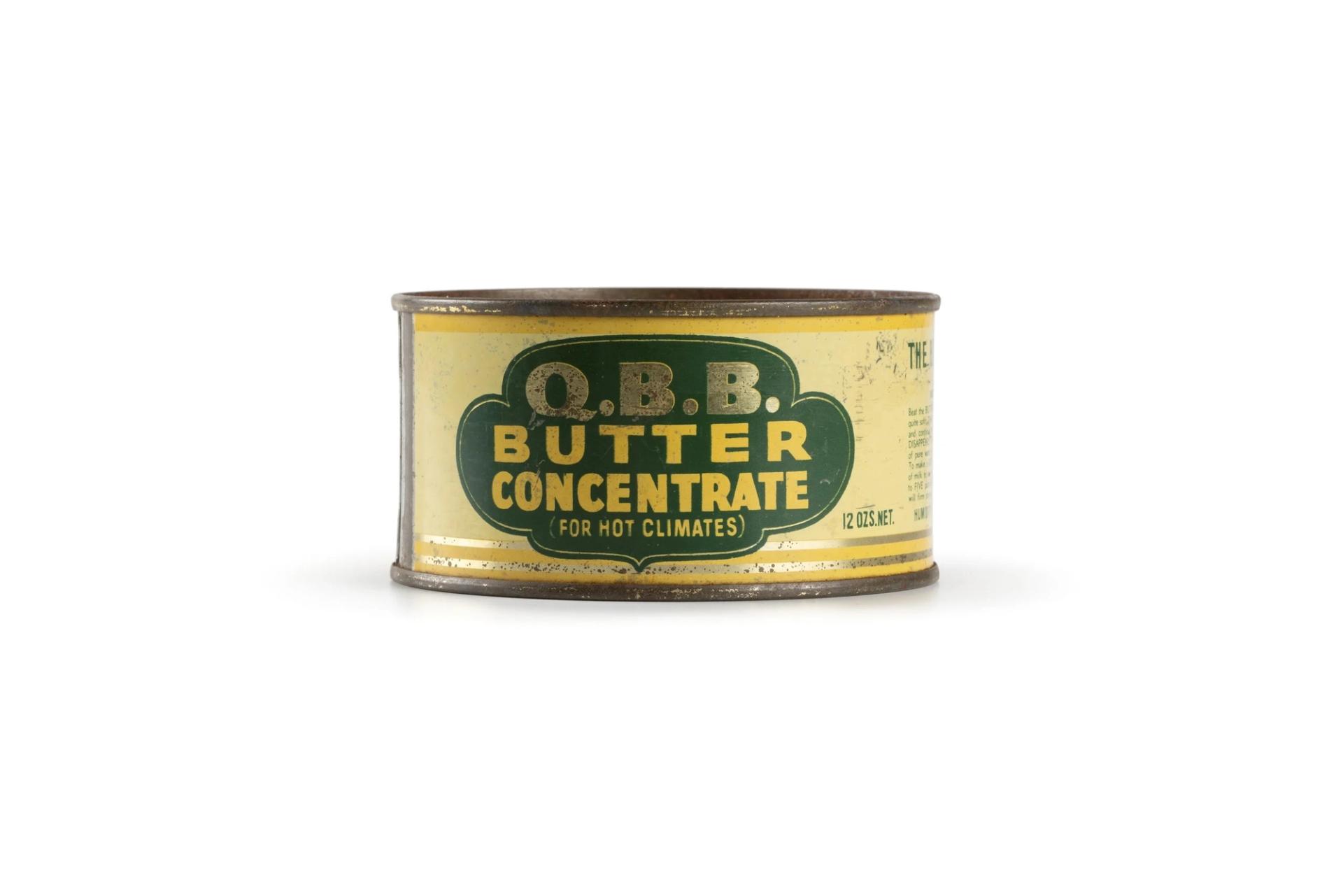 A cylindrical shaped tin-plate can with yellow and green paper label. Text on label reads: 'Q.B.B. / BUTTER / CONCENTRATE / FOR HOT CLIMATES'.