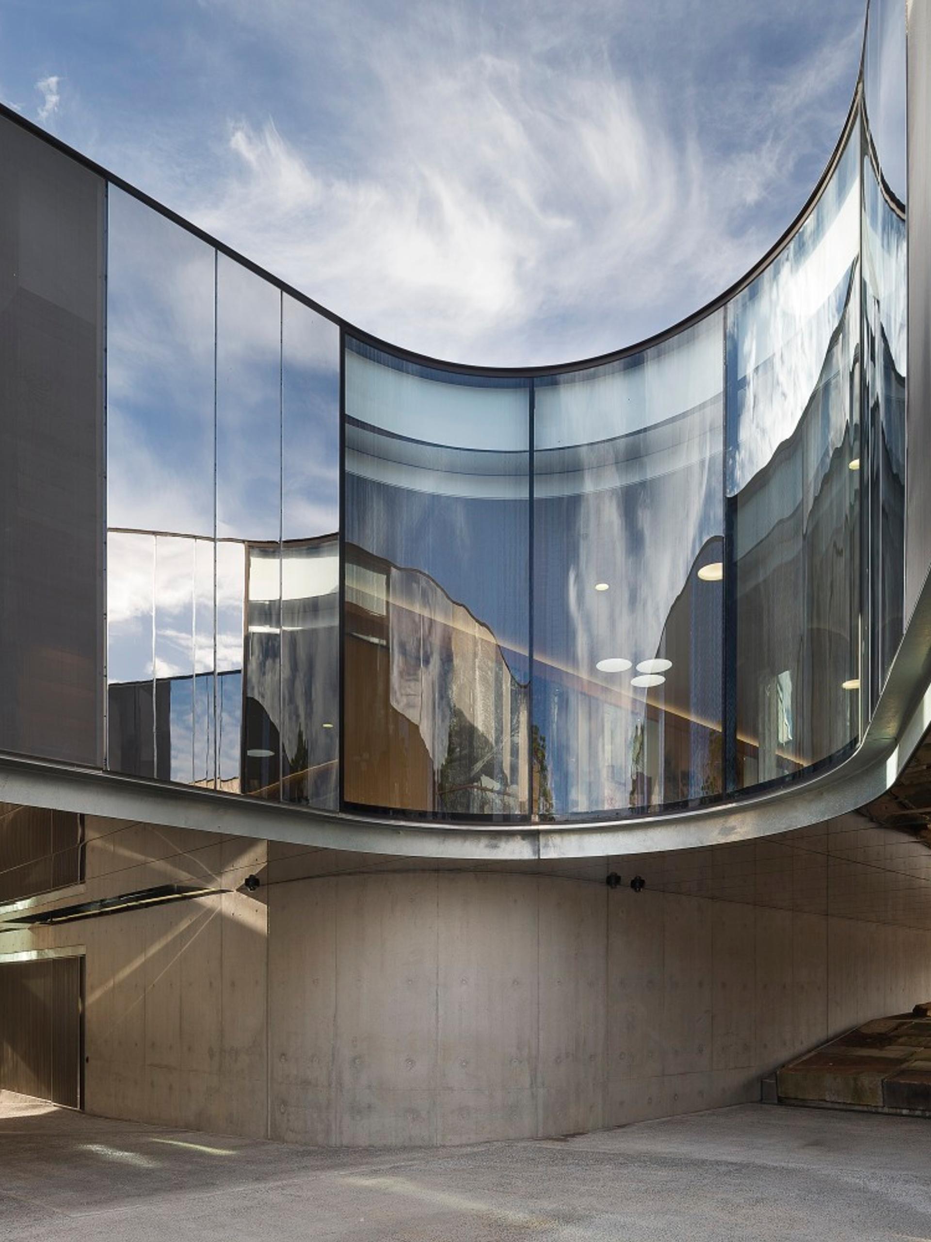 The curving cement, steel and glass exterior of the Australian PlantBank under a bright blue sky. The sky reflects on the building’s partially mirrored surfaces.
