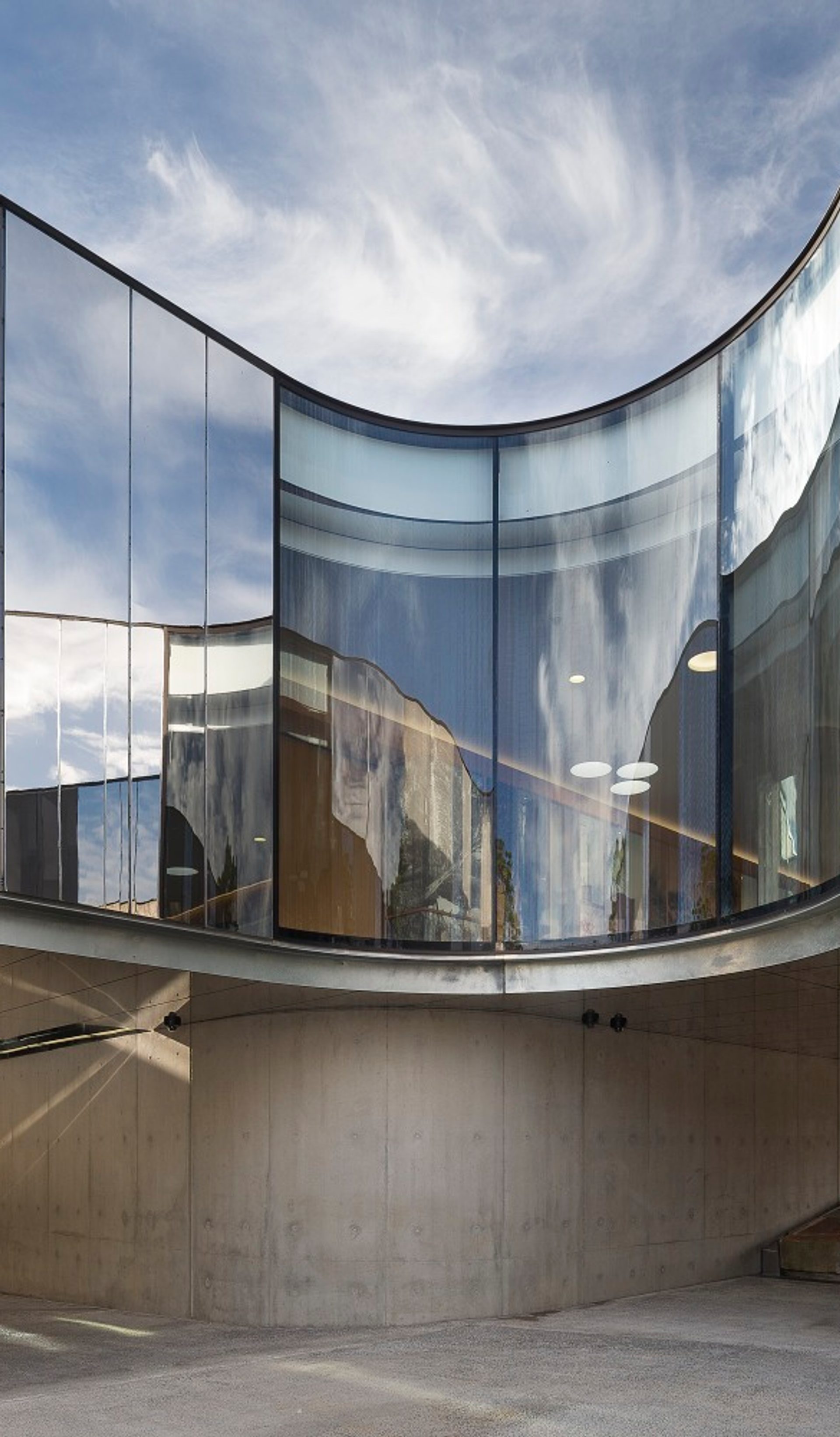 The curving cement, steel and glass exterior of the Australian PlantBank under a bright blue sky. The sky reflects on the building’s partially mirrored surfaces.