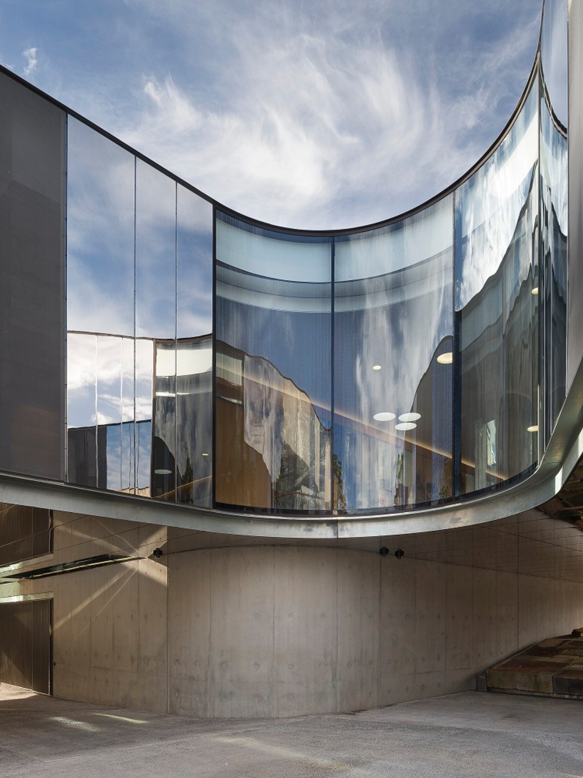 The curving cement, steel and glass exterior of the Australian PlantBank under a bright blue sky. The sky reflects on the building’s partially mirrored surfaces.
