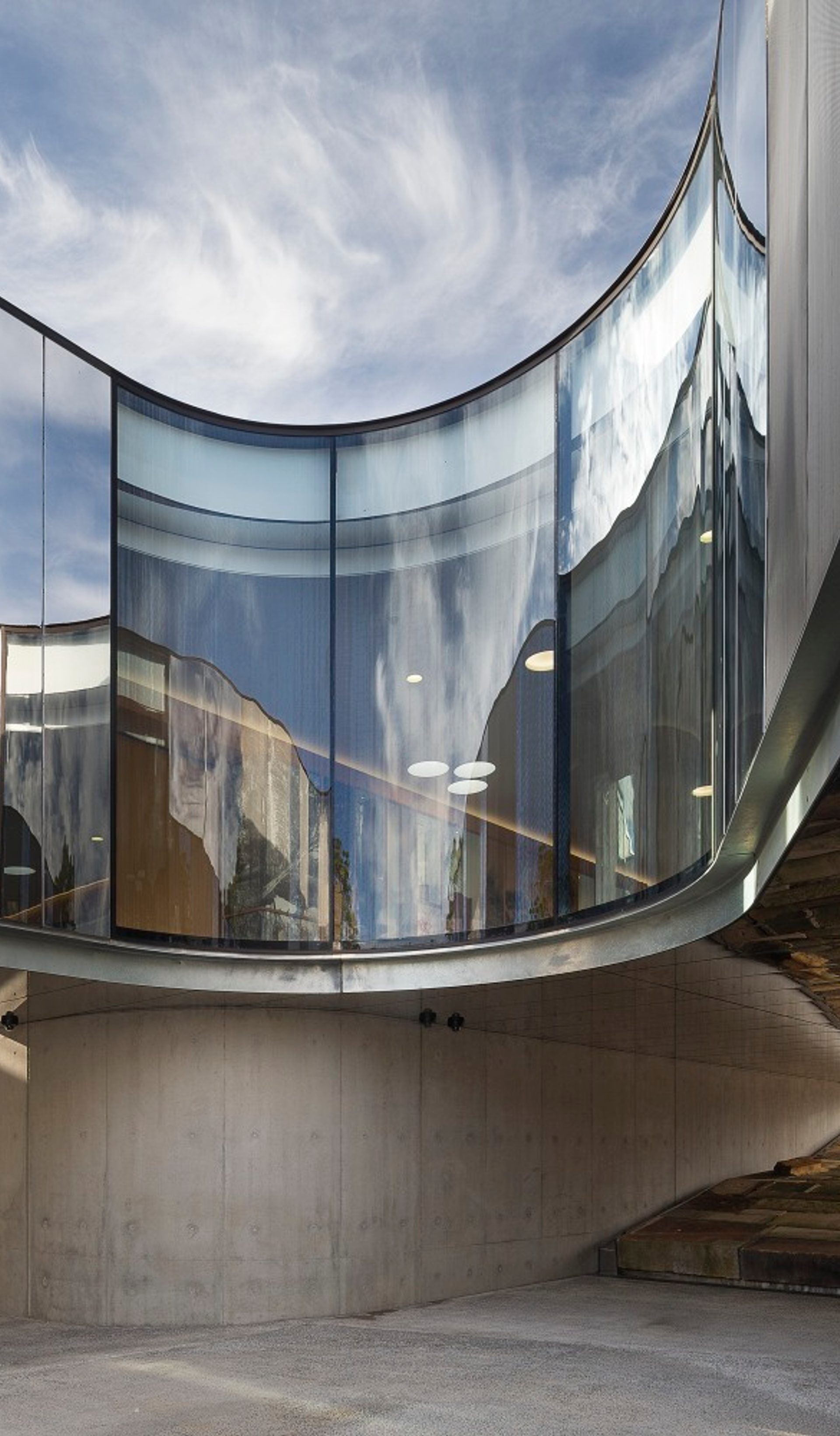 The curving cement, steel and glass exterior of the Australian PlantBank under a bright blue sky. The sky reflects on the building’s partially mirrored surfaces.