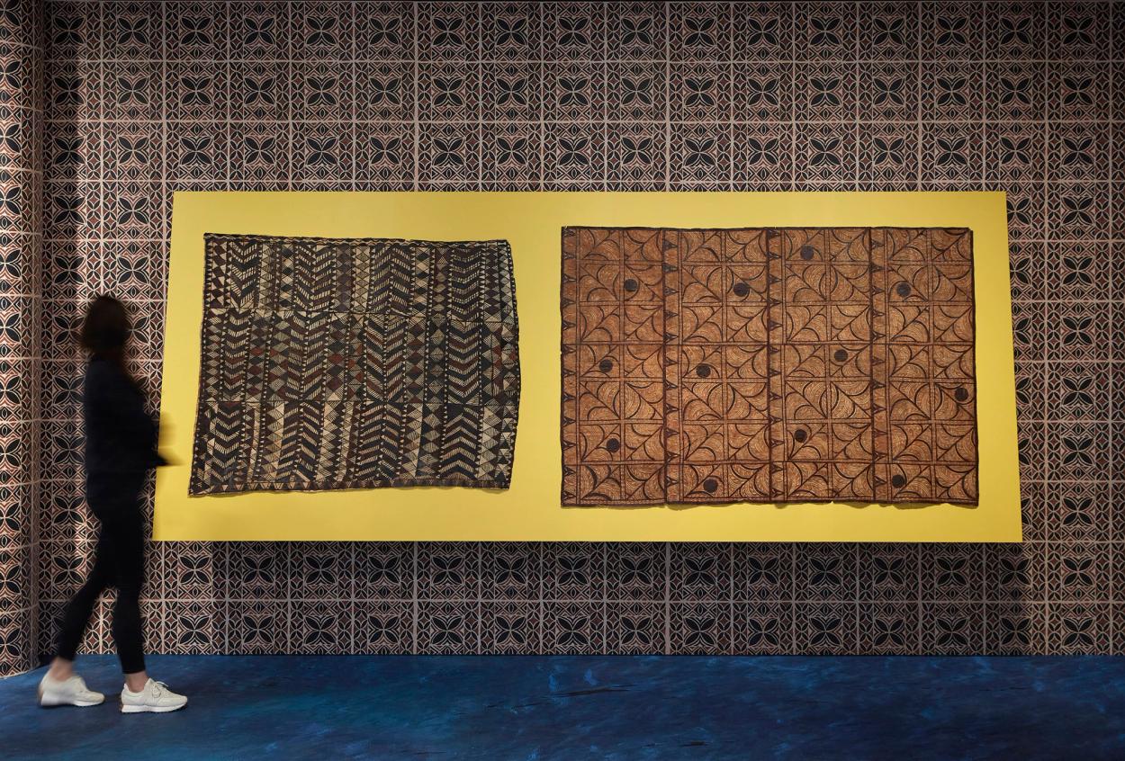 Two siapo (Sāmoan bark cloth) mounted on yellow board.