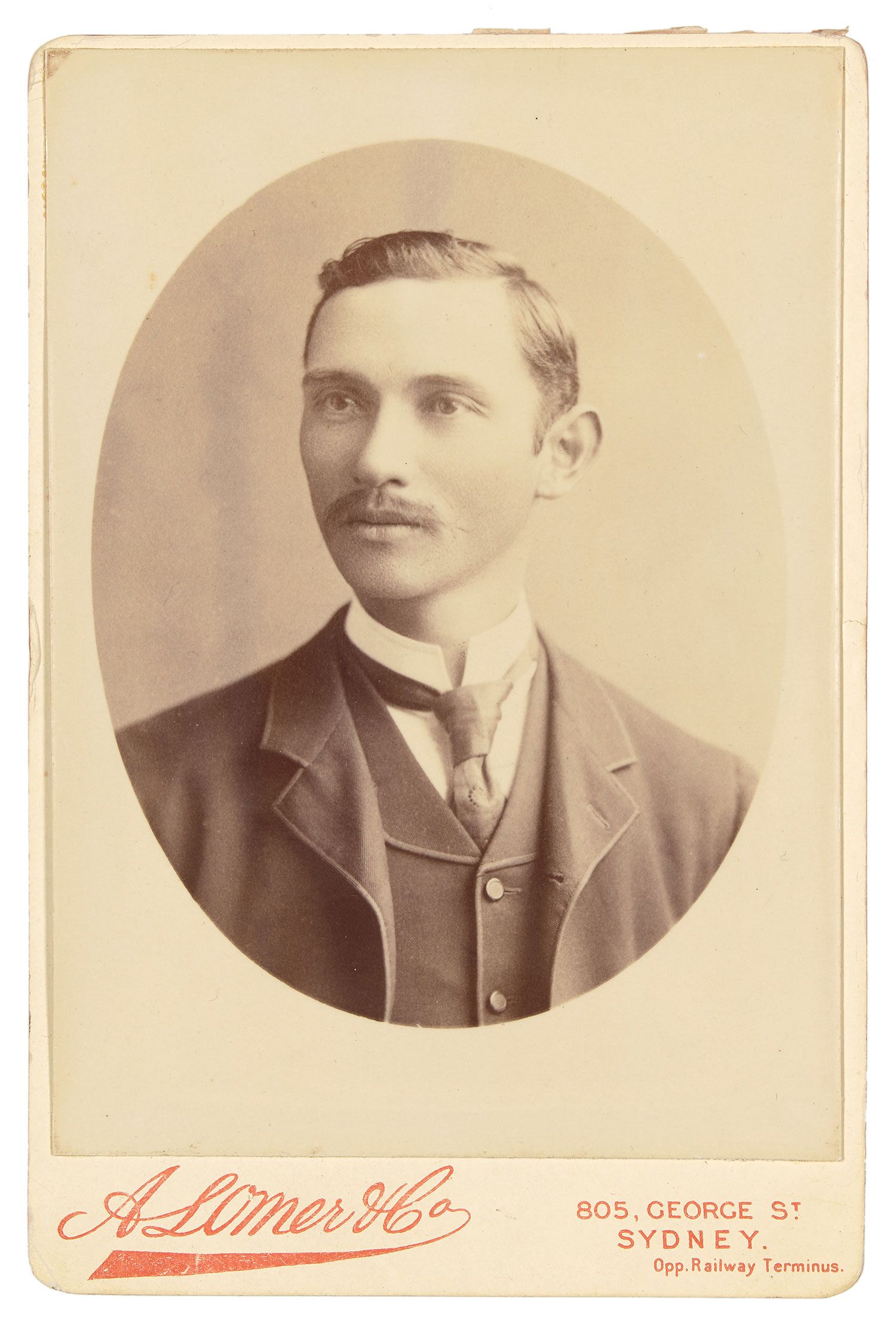 Mounted black and white photograph depicting a man with a moustache wearing a suit with a tie and jacket.