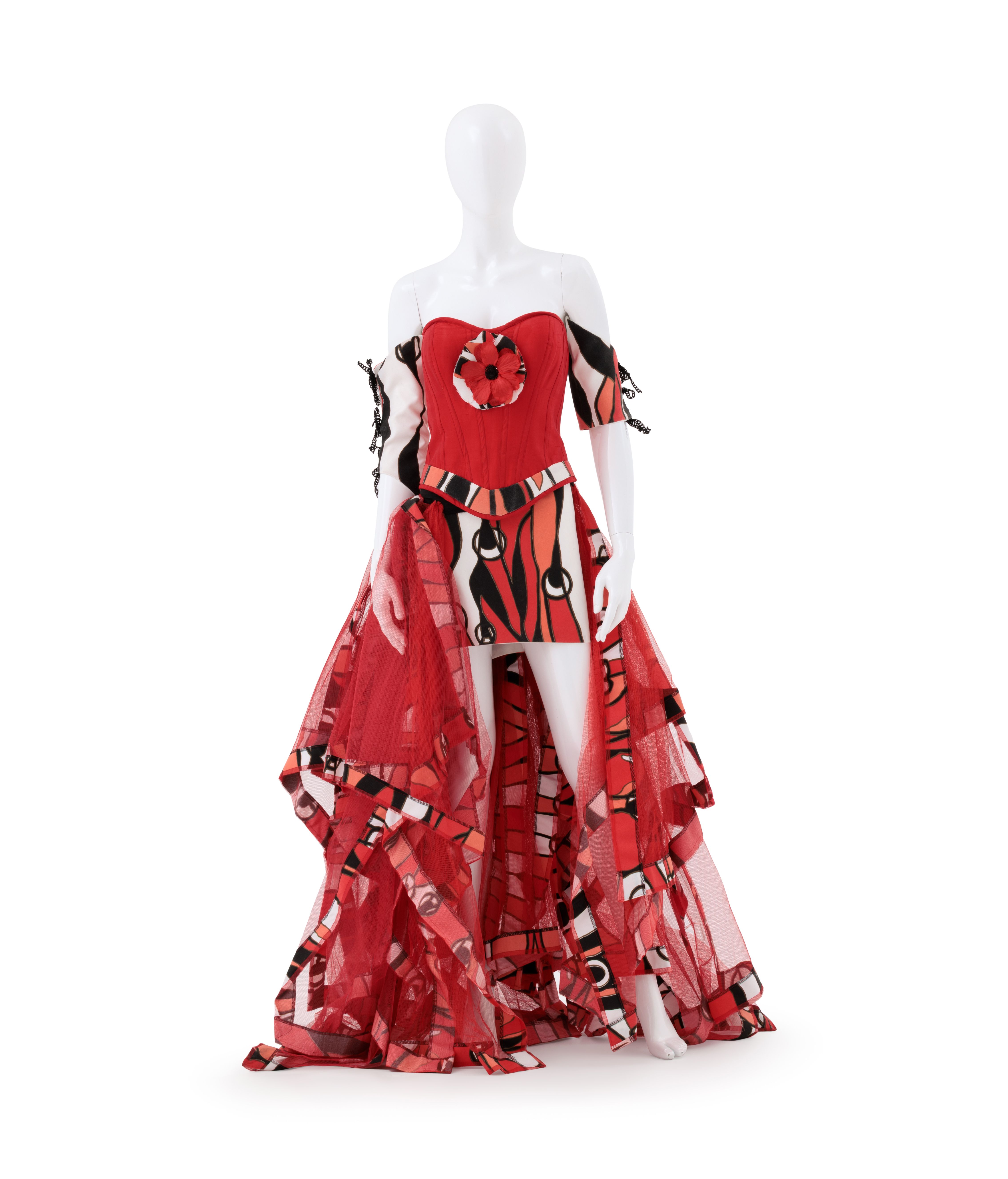 Dress is made in a red, orange, white and black fabric and features red tulle. The fabric pattern is a Signature Prints design by Robyn Caughlan. The dress is an off-the-shoulder design, with a bodice, miniskirt, tulle trail and a pair of arm sleeves. The bodice features a flower at its centre.