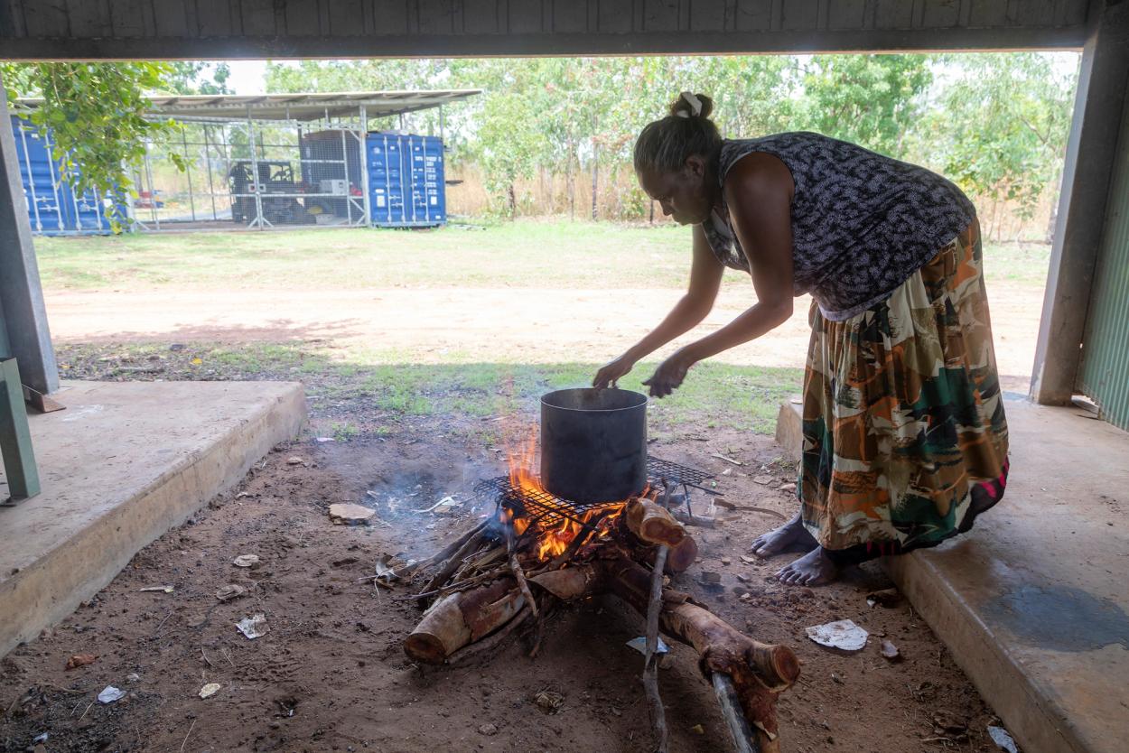 Woman tends to boiling put atop a log fire
