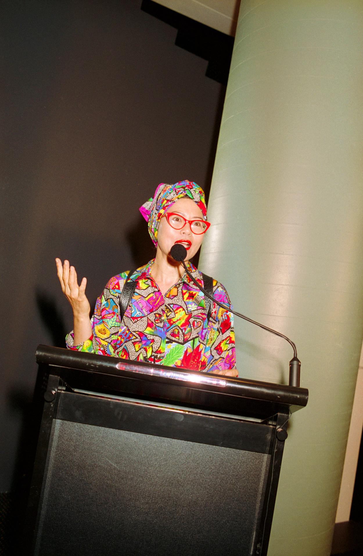 Figure talking behind a podium and microphone.