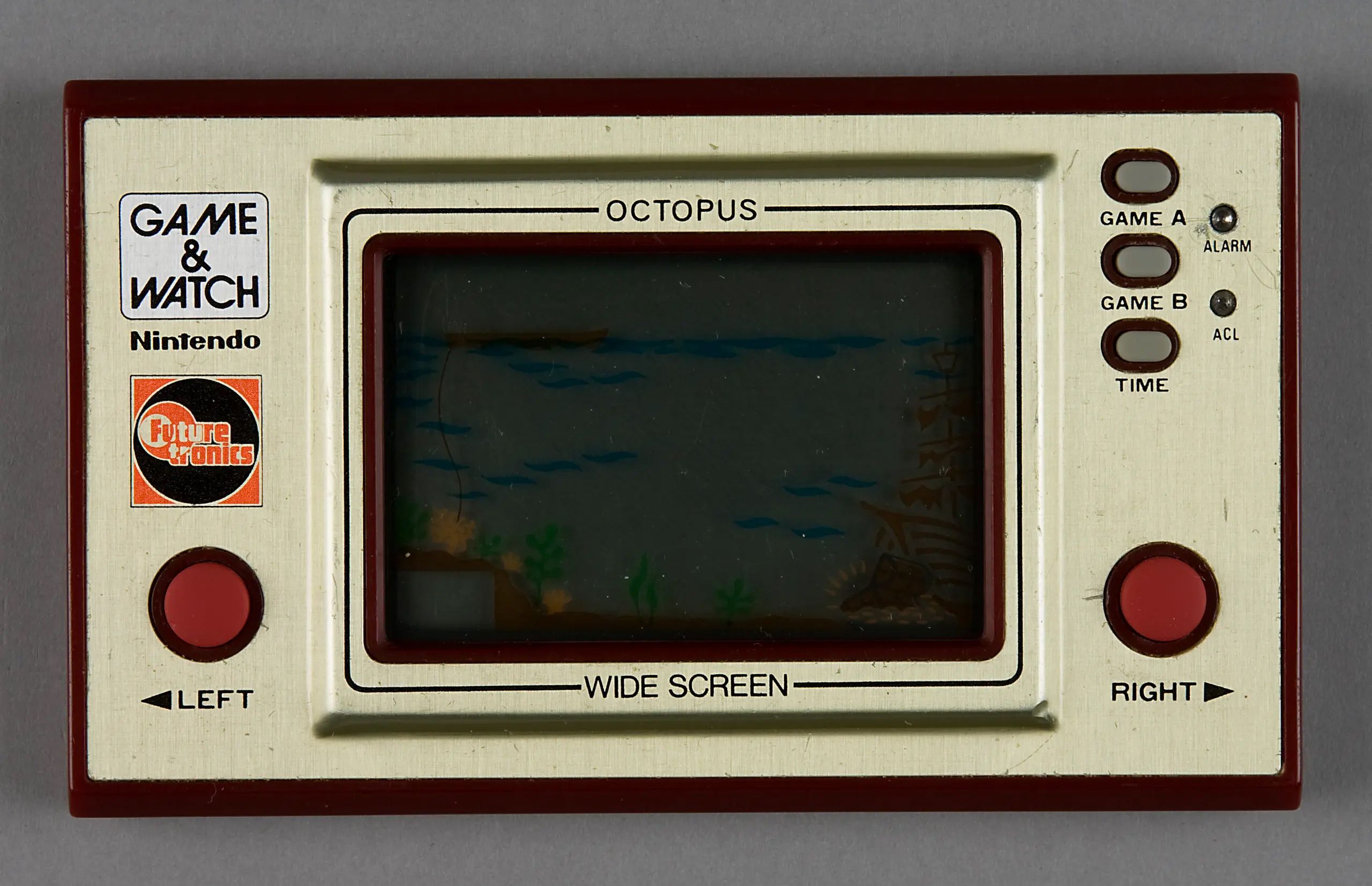 The Octopus Game & Watch console is designed to be held comfortably in both hands and operated with the game controls under the thumbs. It is rectangular and has a maroon plastic casing with gold metallic front. It has an LCD screen in the middle of the front face which has permanent graphics incorporated. The LCD characters move through this display. The control buttons are red and there is a small metal stand at the back. Battery casing at the back.