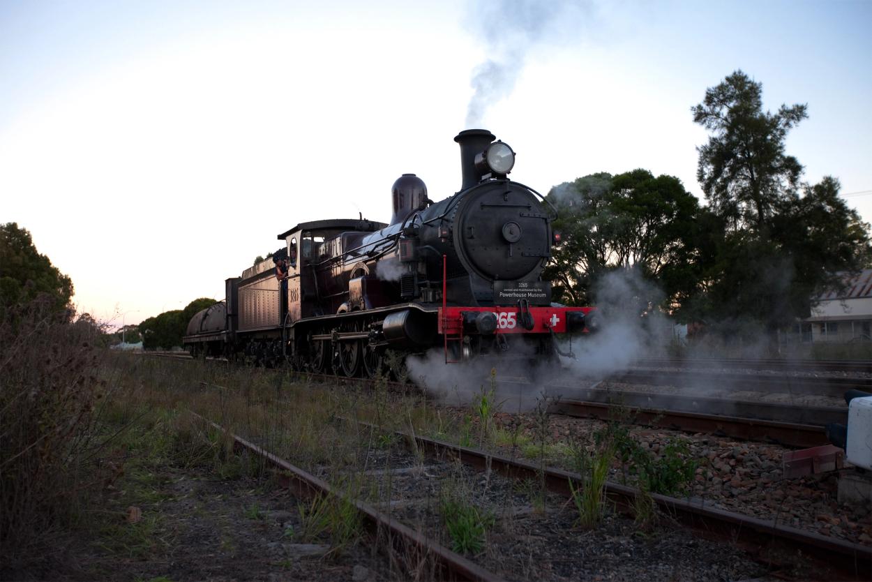 Colour photograph of steam train moving along track at dusk or dawn.