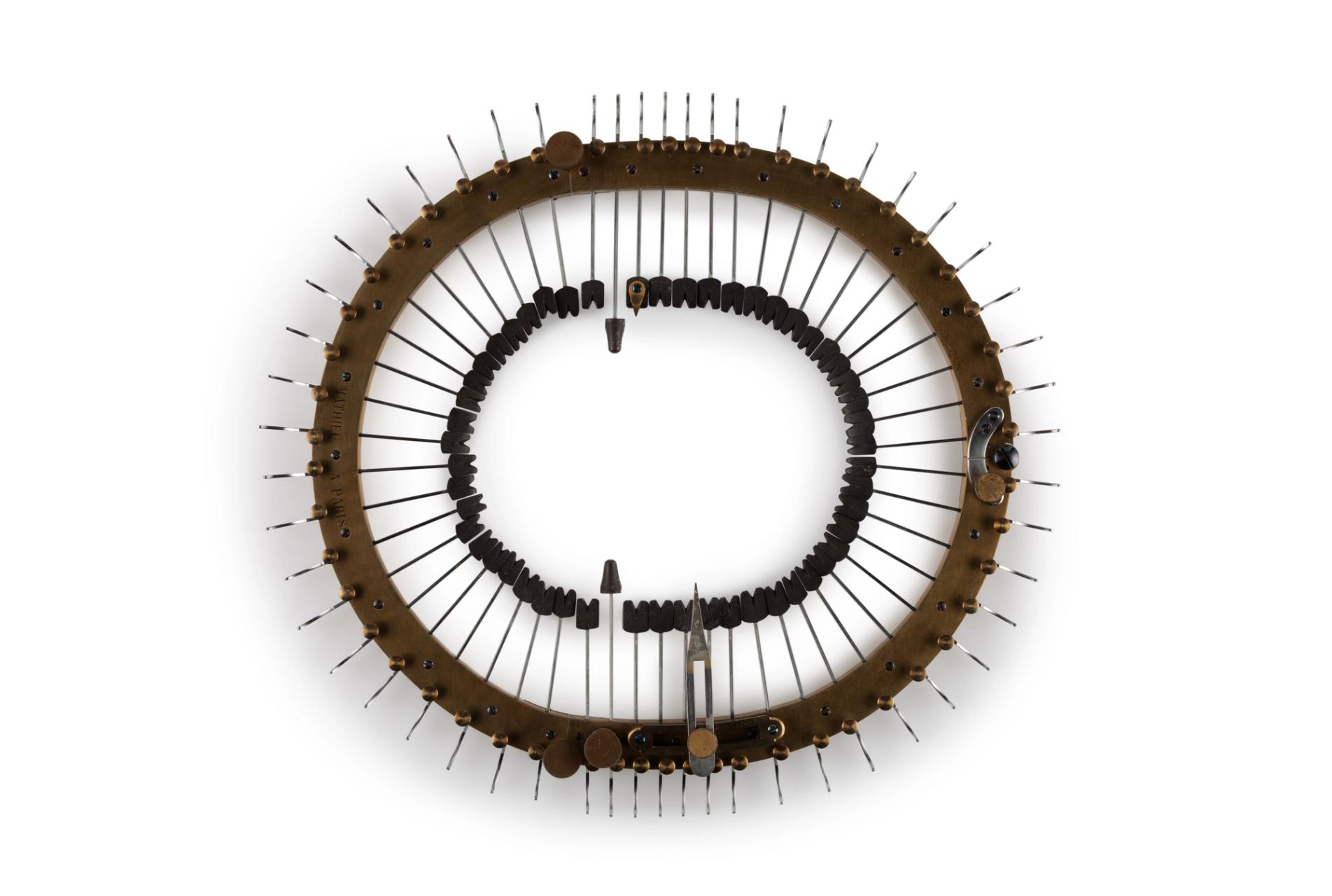 Oval brass frame holding 52 steel spokes (under tension) that are inserted through frame towards centre. The steel spokes have black rectangular ends with incised "V" and are tipped with a rigid natural latex known as gutta percha. They are adjusted by means of buttons to ratchet and spring. A component of the craniometer is a detachable steel strip that fits over the skull. There is also a lead pencil in a pencil holder with brass and metal attachment, and a nail with a brass head.
