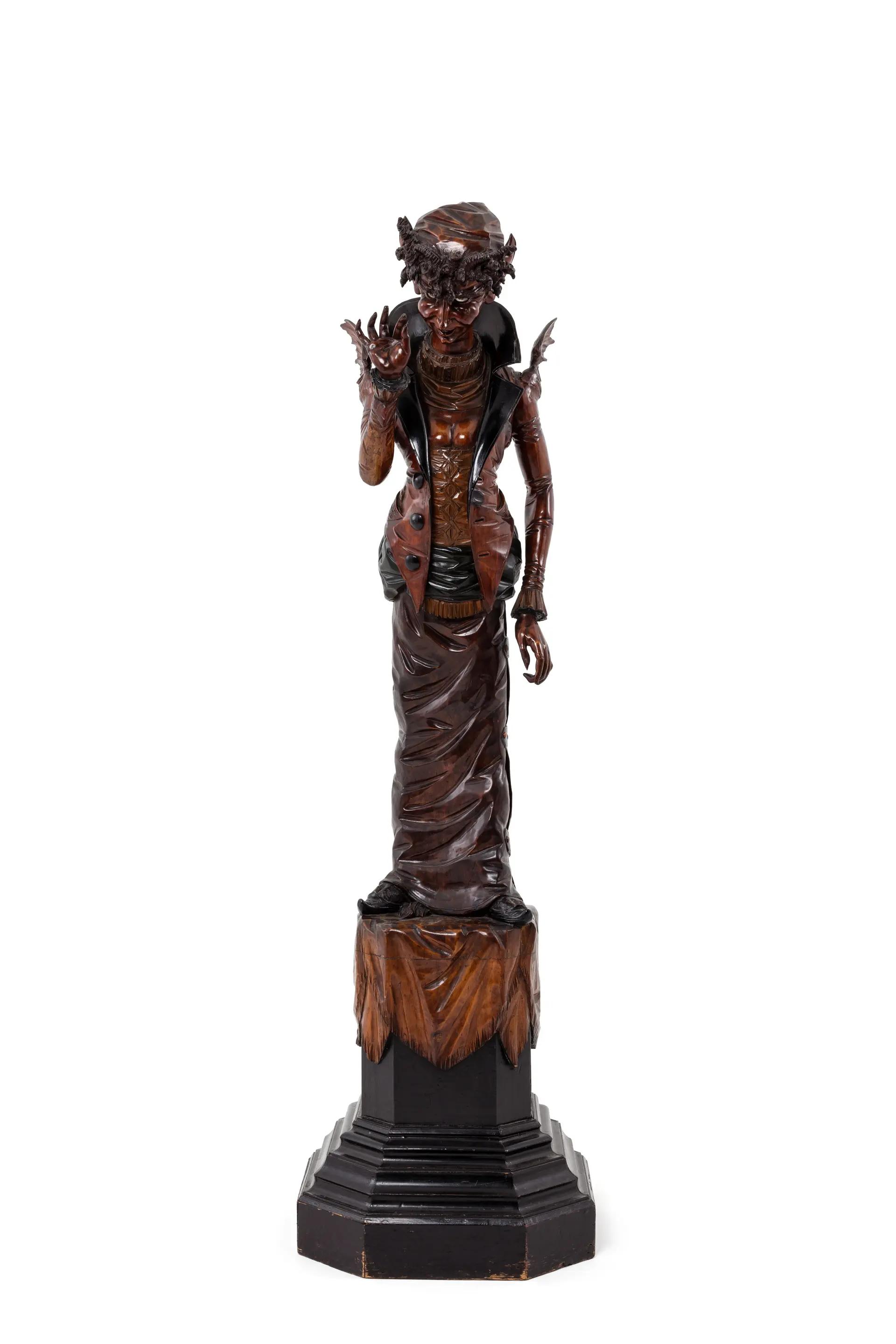 Carved pine wood figure of a standing female, faun-like being dressed in an interpretation of late 1800s women's fashion standing on a 600mm high stepped octagonal pedestal, the upper section with carved drapery. On its pedestal, the figure stands almost two metres tall and has an exaggerated S-bend posture which pushes the head forward and buttocks out.
