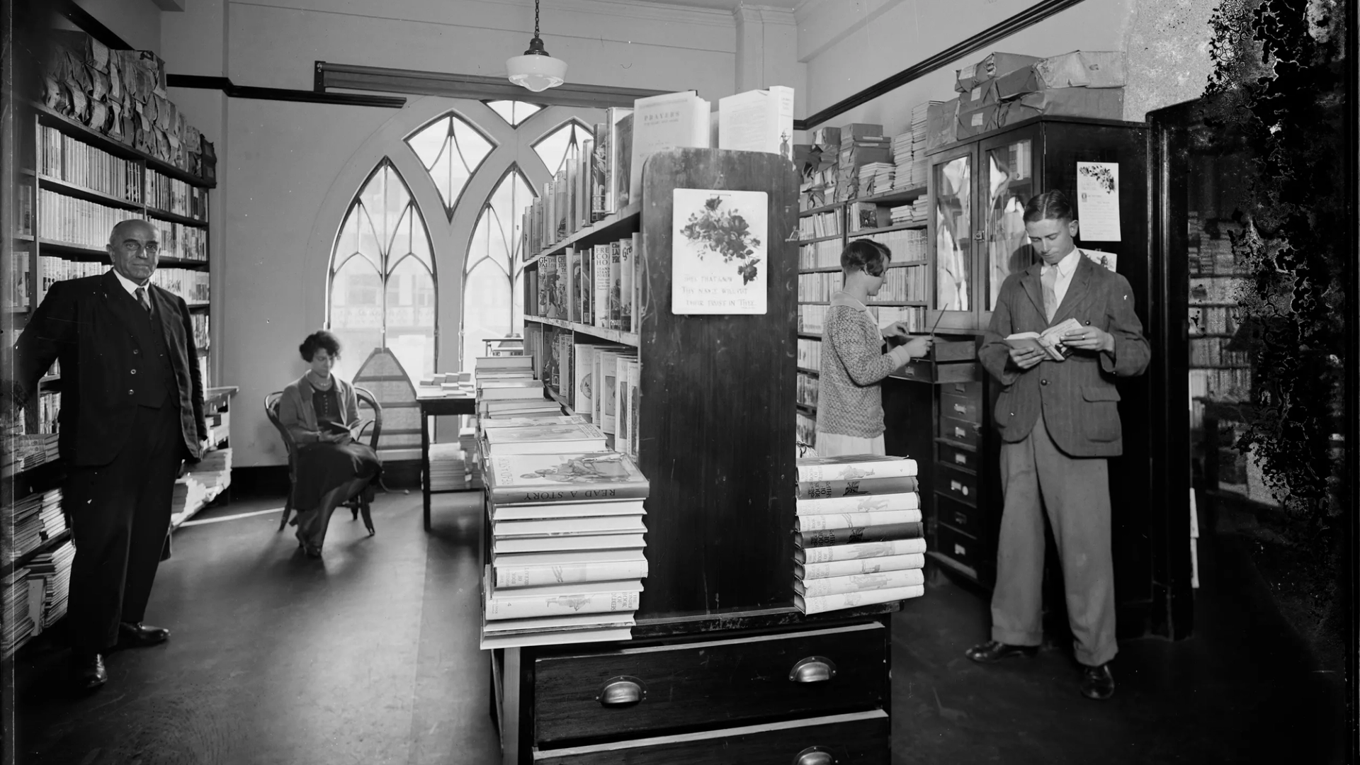 A landscape black and white photograph depicting two men and two women browsing in the book room, later known as the Margaret Street Bookshop.
