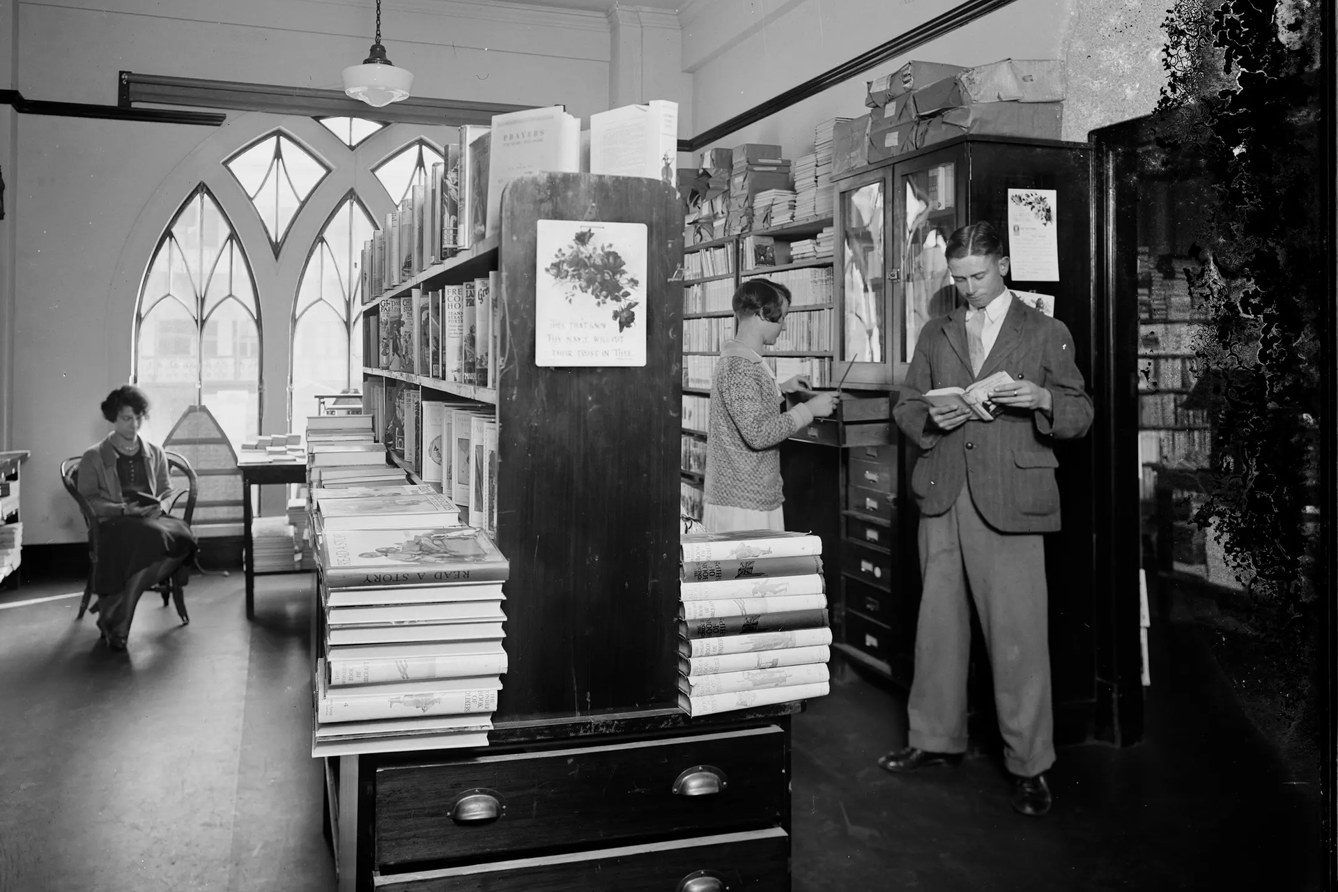A landscape black and white photograph depicting two men and two women browsing in the book room, later known as the Margaret Street Bookshop.
