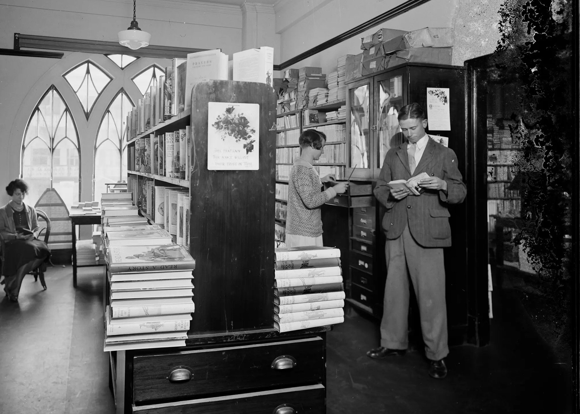 A landscape black and white photograph depicting two men and two women browsing in the book room, later known as the Margaret Street Bookshop.