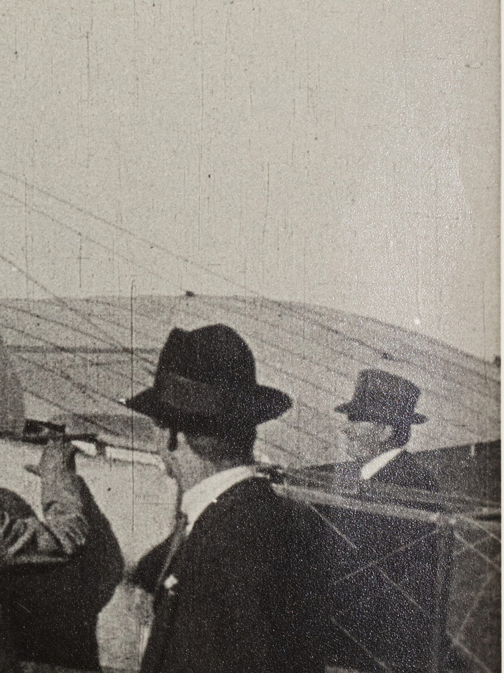 Black and white photograph of the first Australian airmail flight at Government House Melbourne. Multiple men in suits and hats looking to a pilot sitting on a plane, preparing to fly.