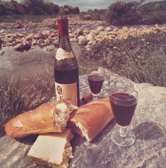 Photographic print, colour, for Qantas advertisement on paper. Red wine, bread and cheese on a rock by a river.