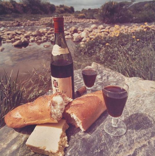 Photographic print, colour, for Qantas advertisement on paper. Red wine, bread and cheese on a rock by a river.