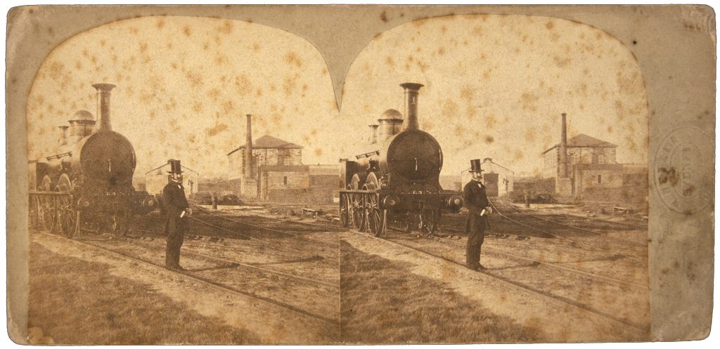 Man in a top hat, from 1877, standing in front of the Locomotive.