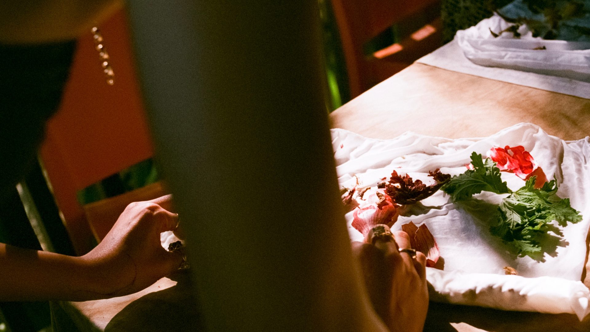 Behind a person's arm they work with organic materials and fabric in the sunlight