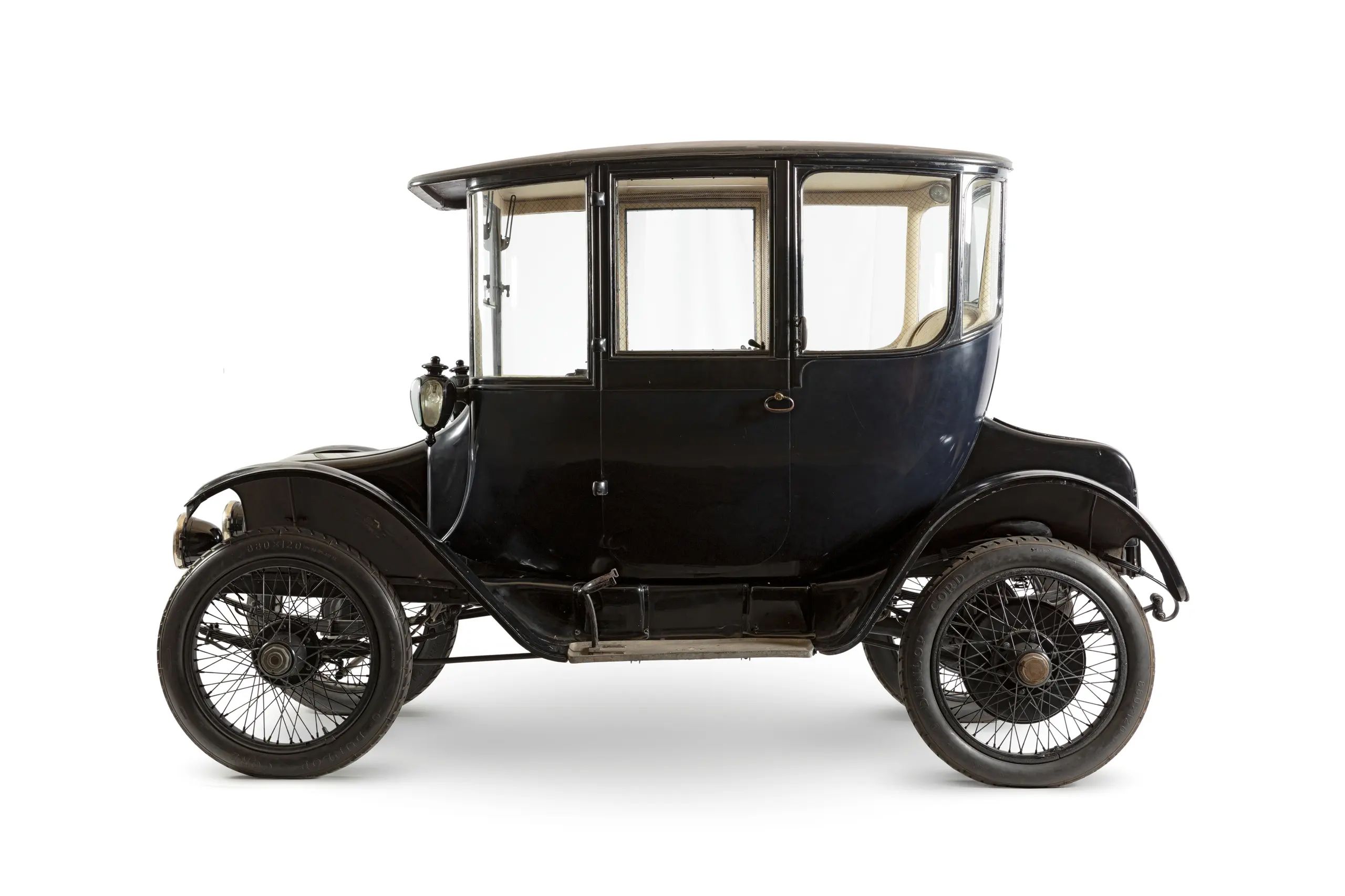 A side image of a full size motor car from the 1910's. The object is finished in black enamel paint and polished to a high shine.