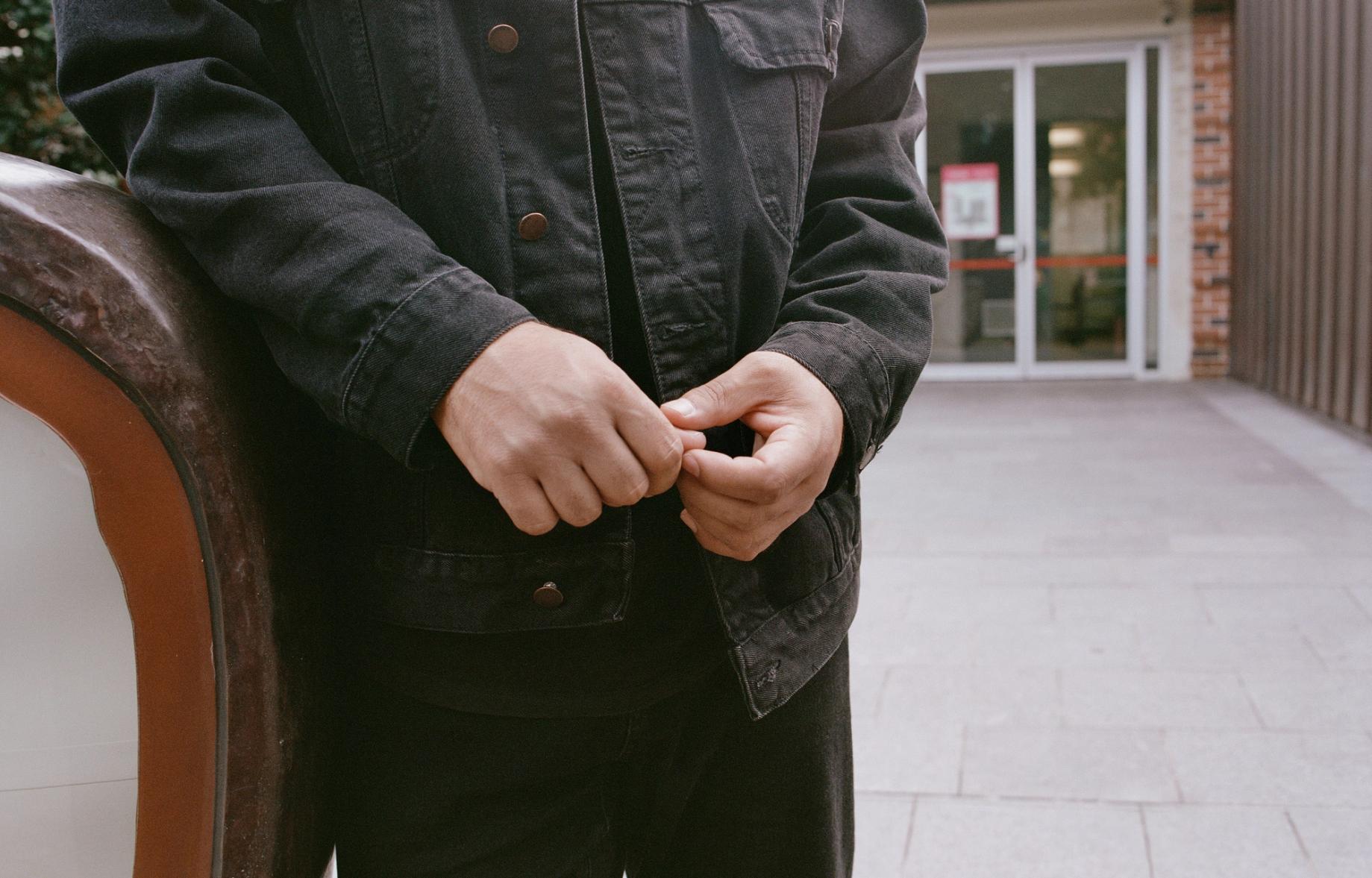 Person leans on an outdoor bench, hands together in front of them.