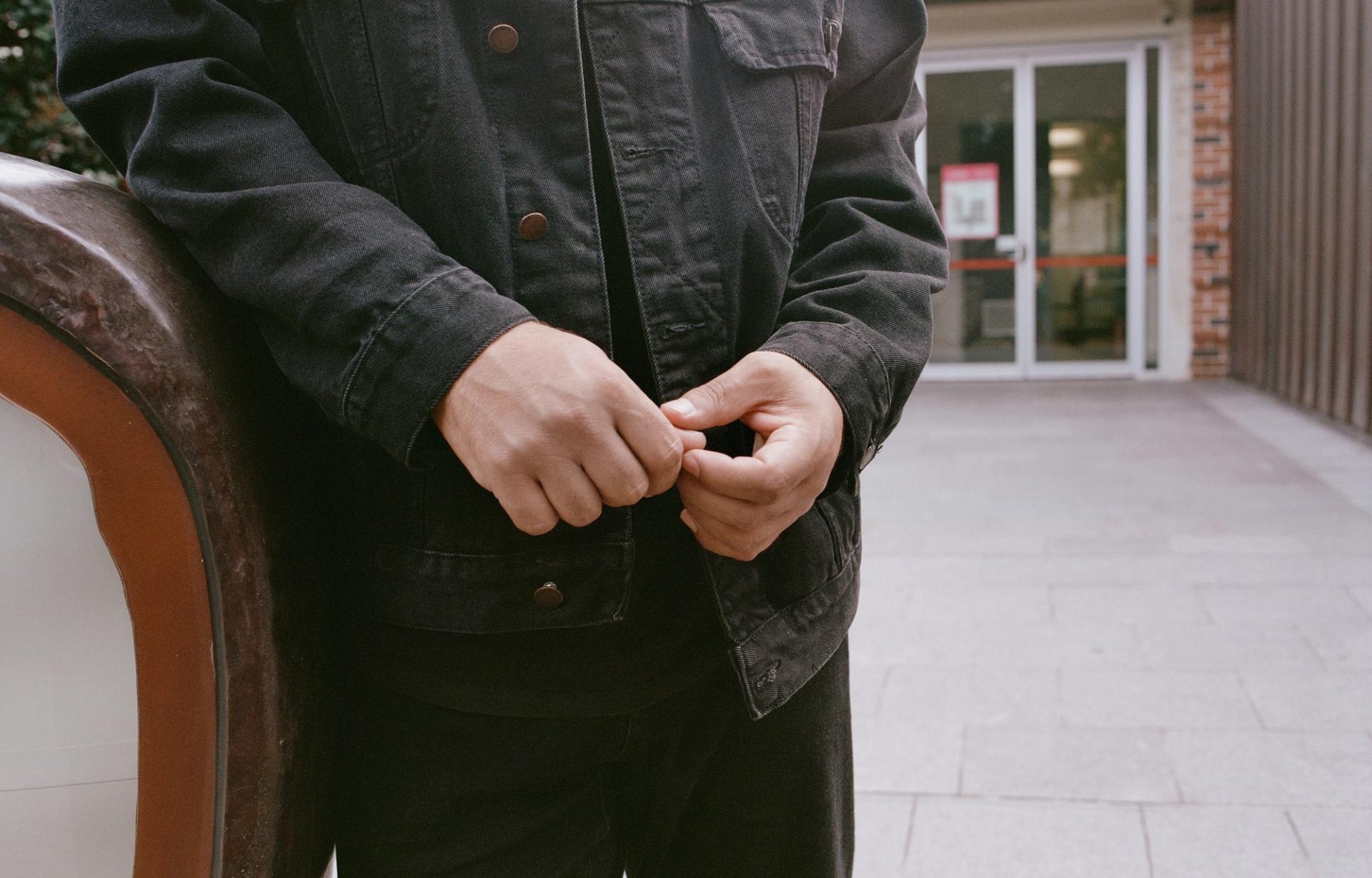 Person leans on an outdoor bench, hands together in front of them.