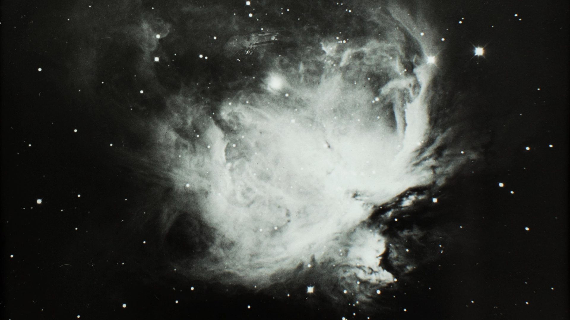Black and white image of the great nebulae in Orion, space sky showing stars and a wispy bright cluster in the centre (Orion).