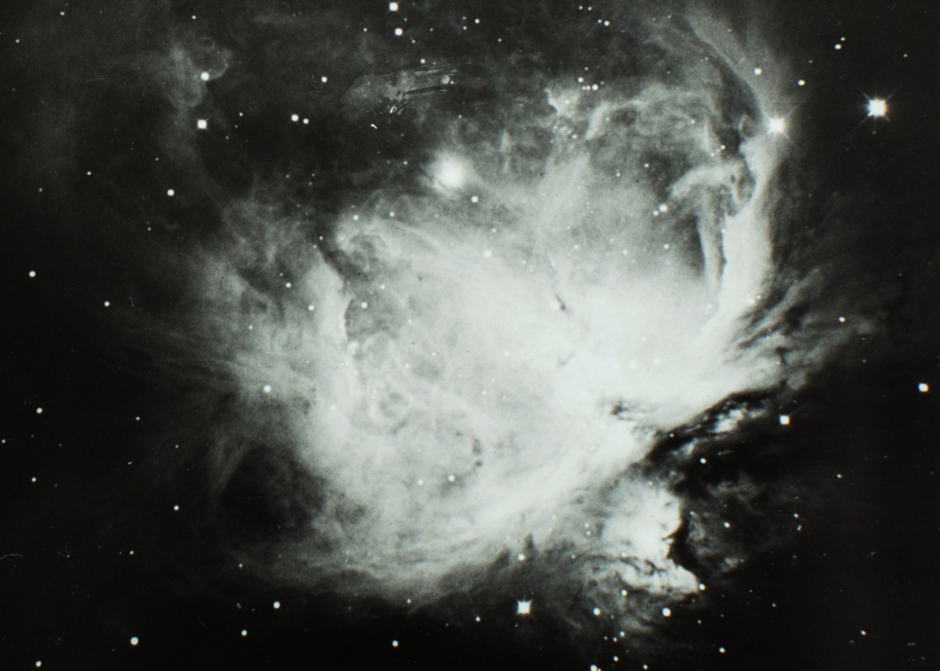 Black and white image of the great nebulae in Orion, space sky showing stars and a wispy bright cluster in the centre (Orion).