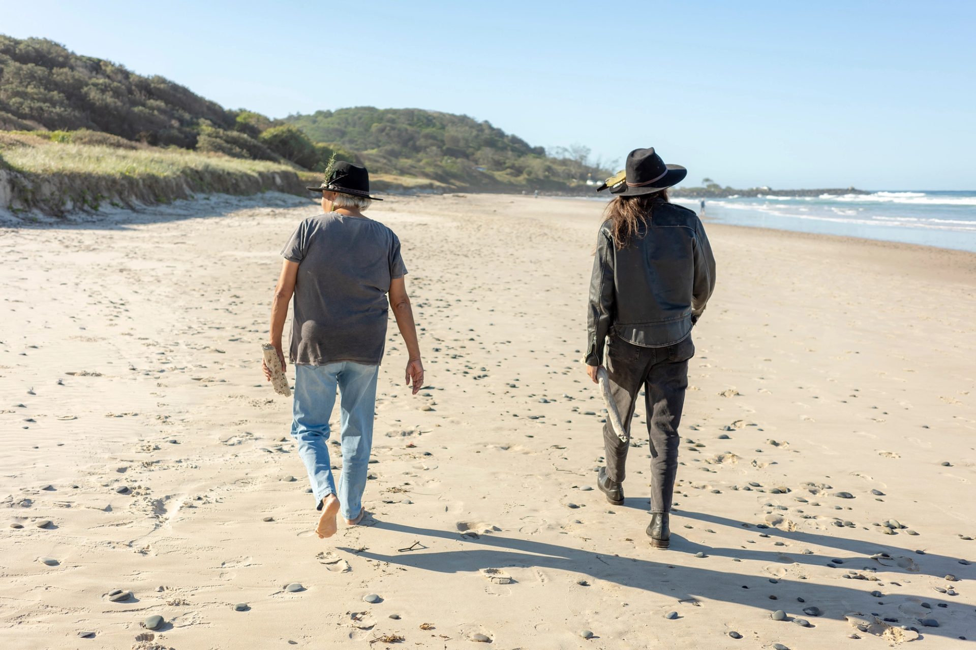 Two women walking on a beach with their backs to the camera.