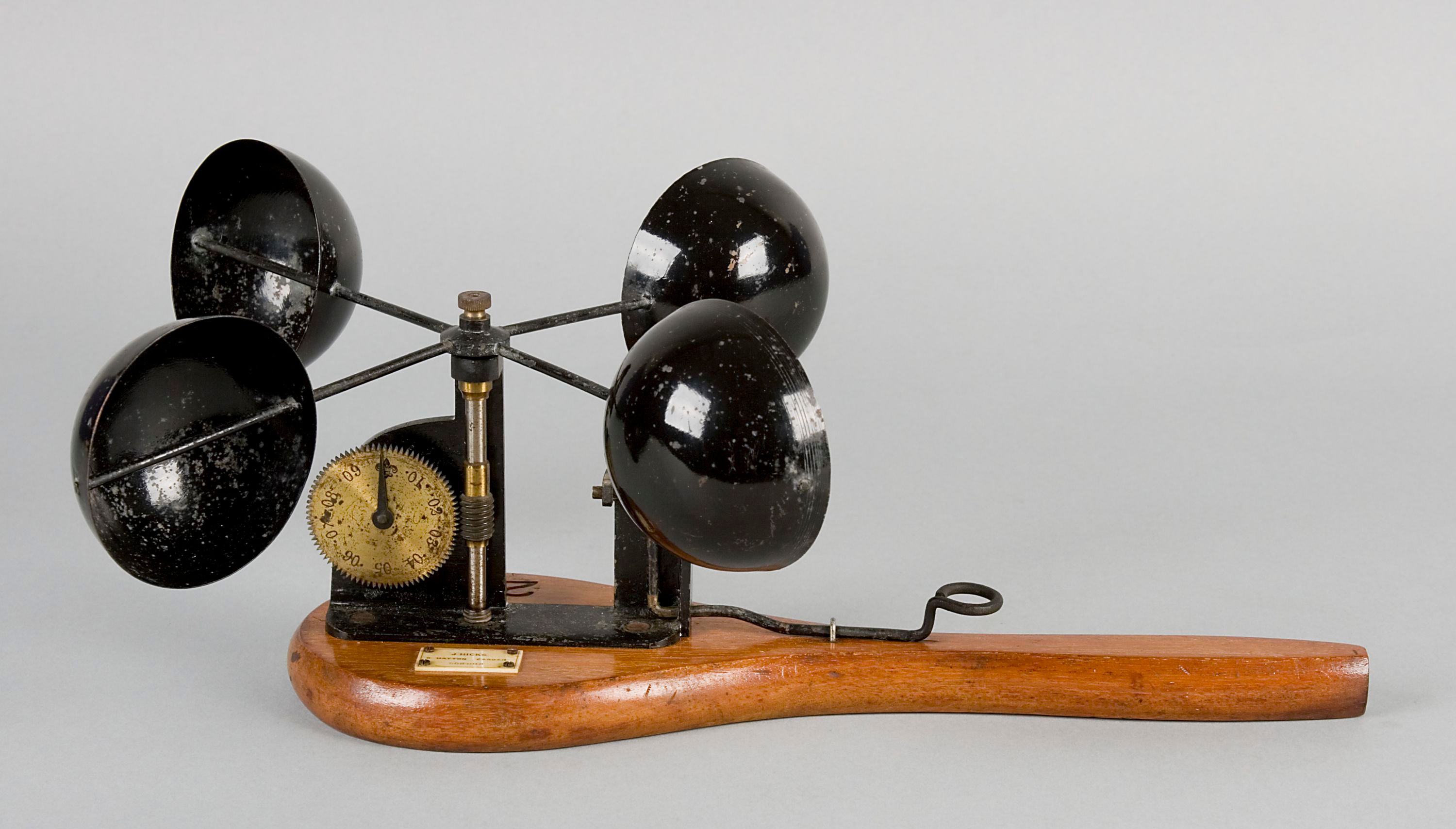 Hand-held anemometer with four hollow hemispherical cups fixed to rotating cross arms that are mounted on a flat, paddle-shaped wooden base.
