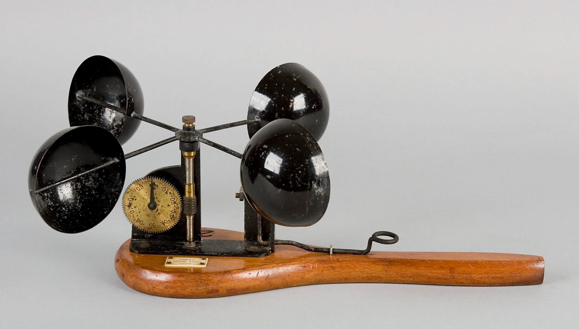 Hand-held anemometer with four hollow hemispherical cups fixed to rotating cross arms that are mounted on a flat, paddle-shaped wooden base.