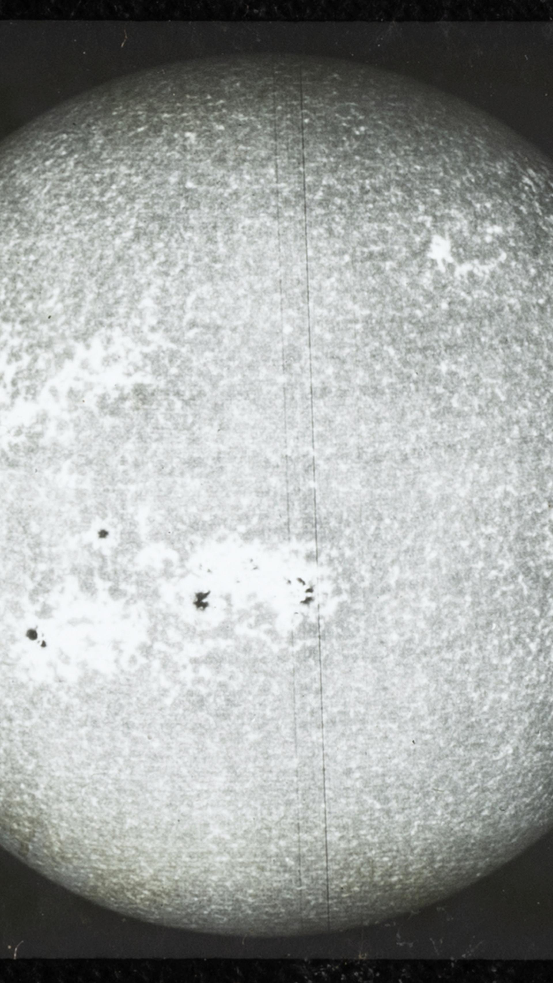 A close up photograph of a glass plate slide showing black and white photo of 'sun's disk (spectroheliogram)', used for teaching astronomy.