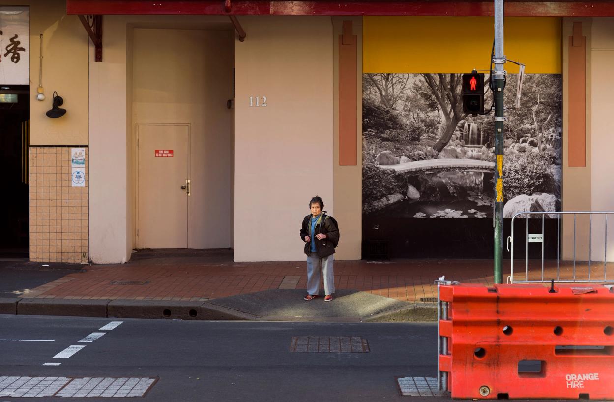 A figure stands at the edge of the footpath waiting to cross the road.