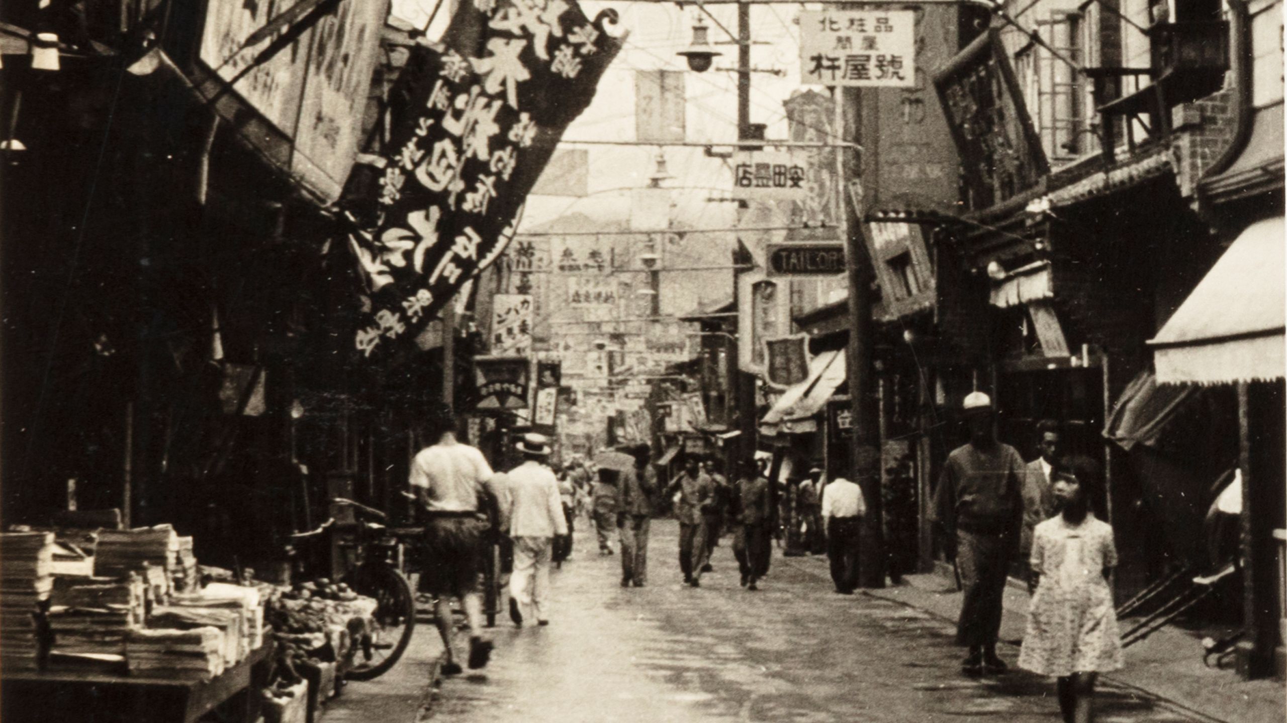 Black and white photograph of a street scene in Keijo, Korea, showing pedestrians walking either side along a banner filled street.