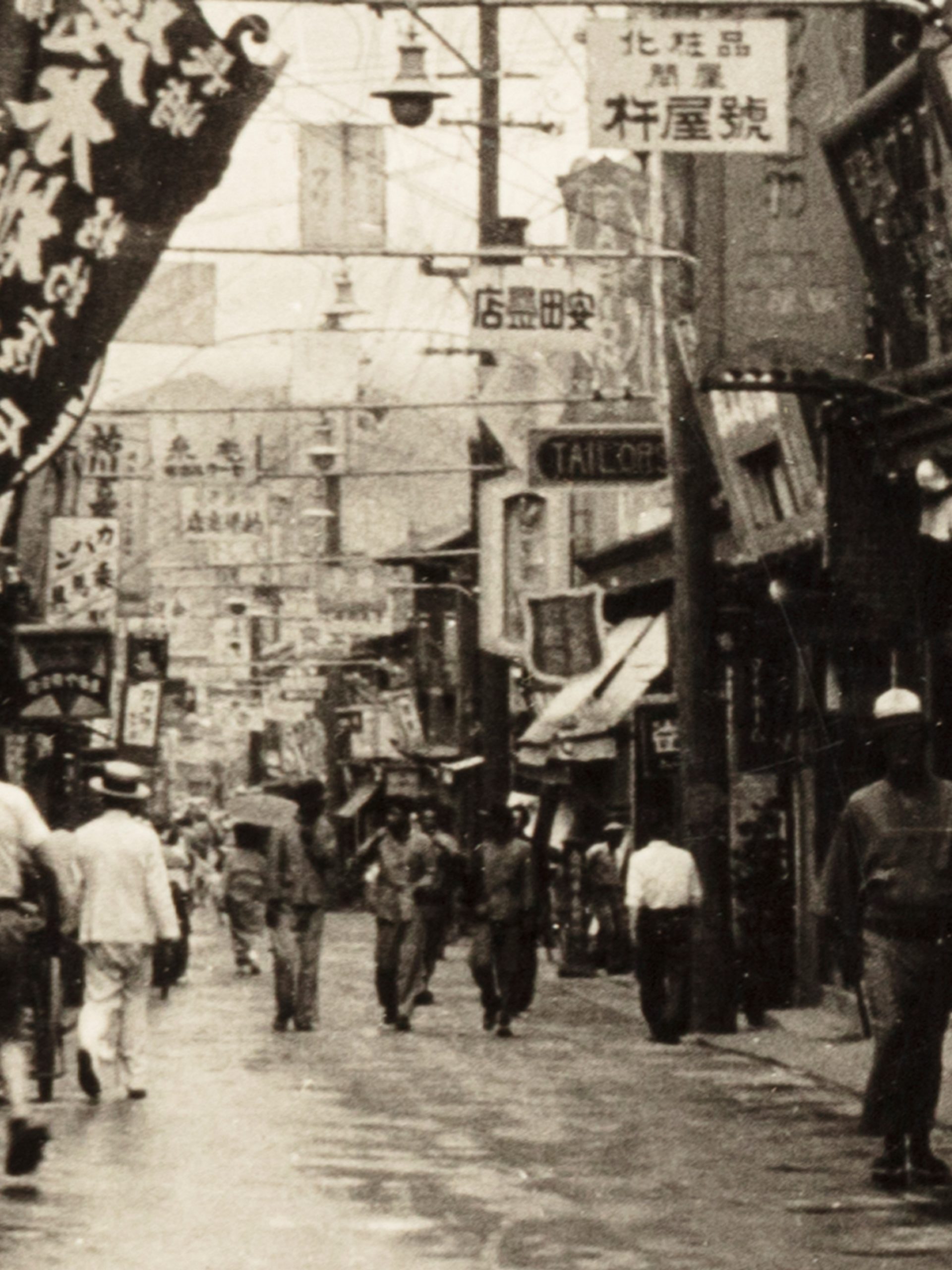 Black and white photograph of a street scene in Keijo, Korea, showing pedestrians walking either side along a banner filled street.